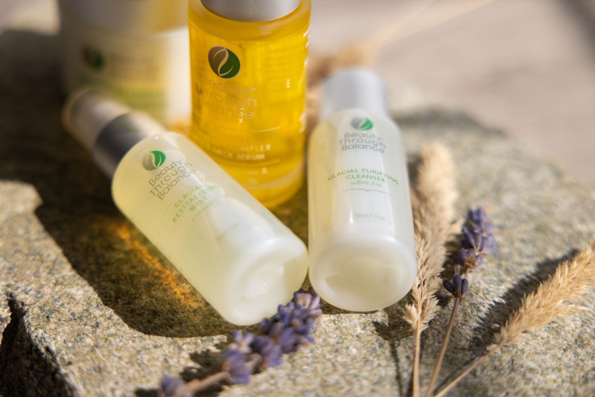 Three white and yellow cosmetic bottles among lavender flowers on a stone surface