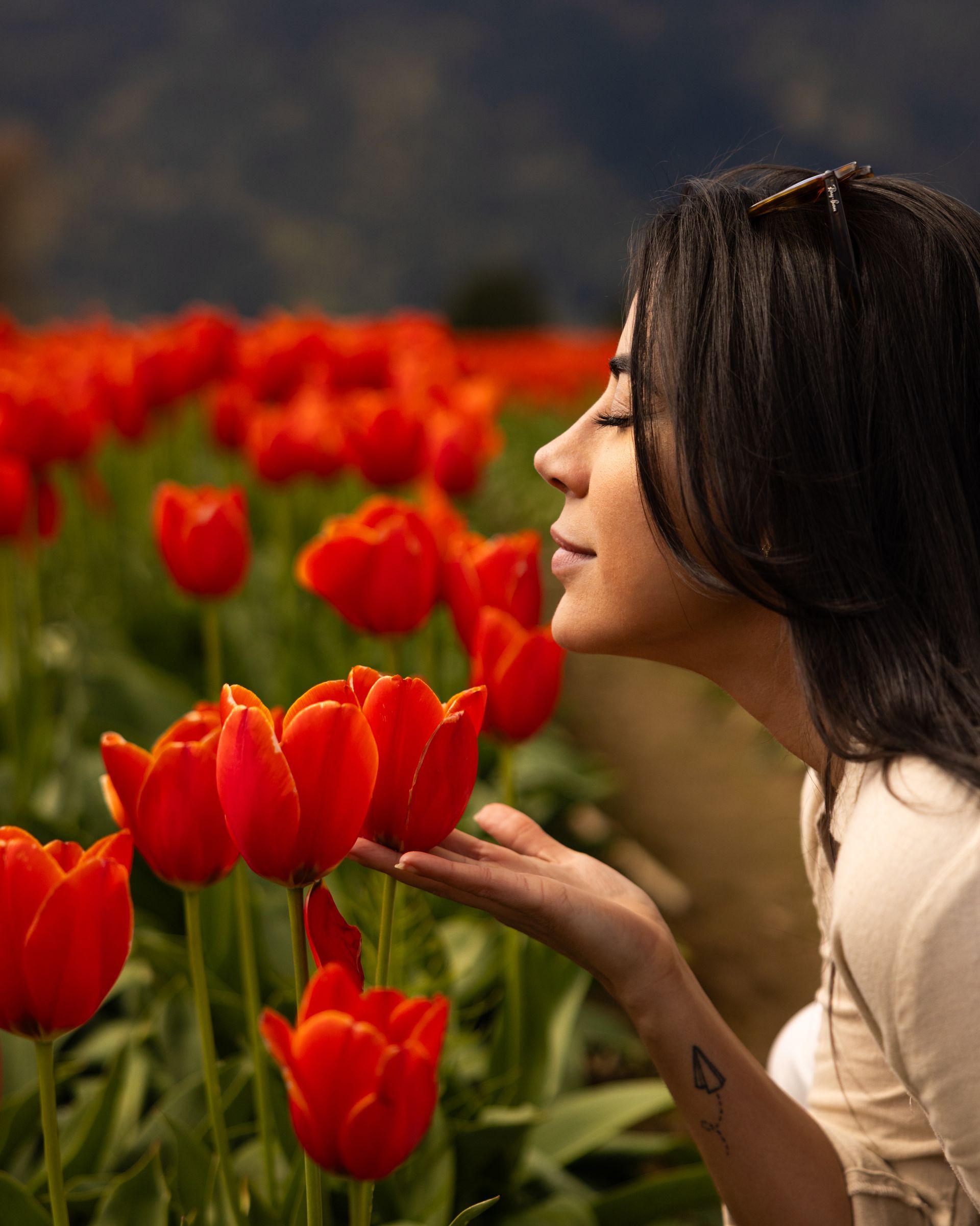 Woman smelling red tulips in a garden, with a blurred field of flowers behind her.
