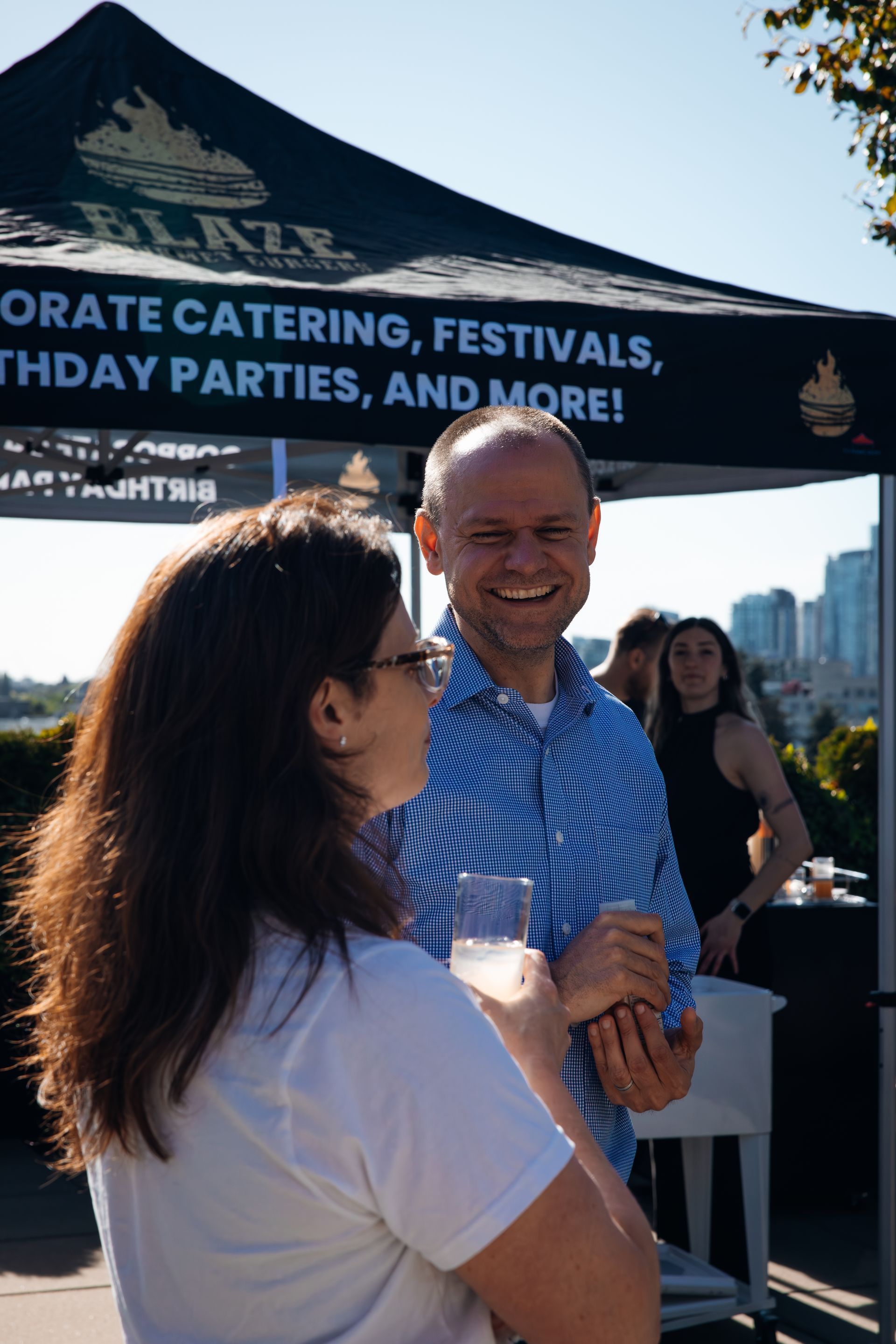 Two people talking under a dark blue event tent at an outdoor festival booth
