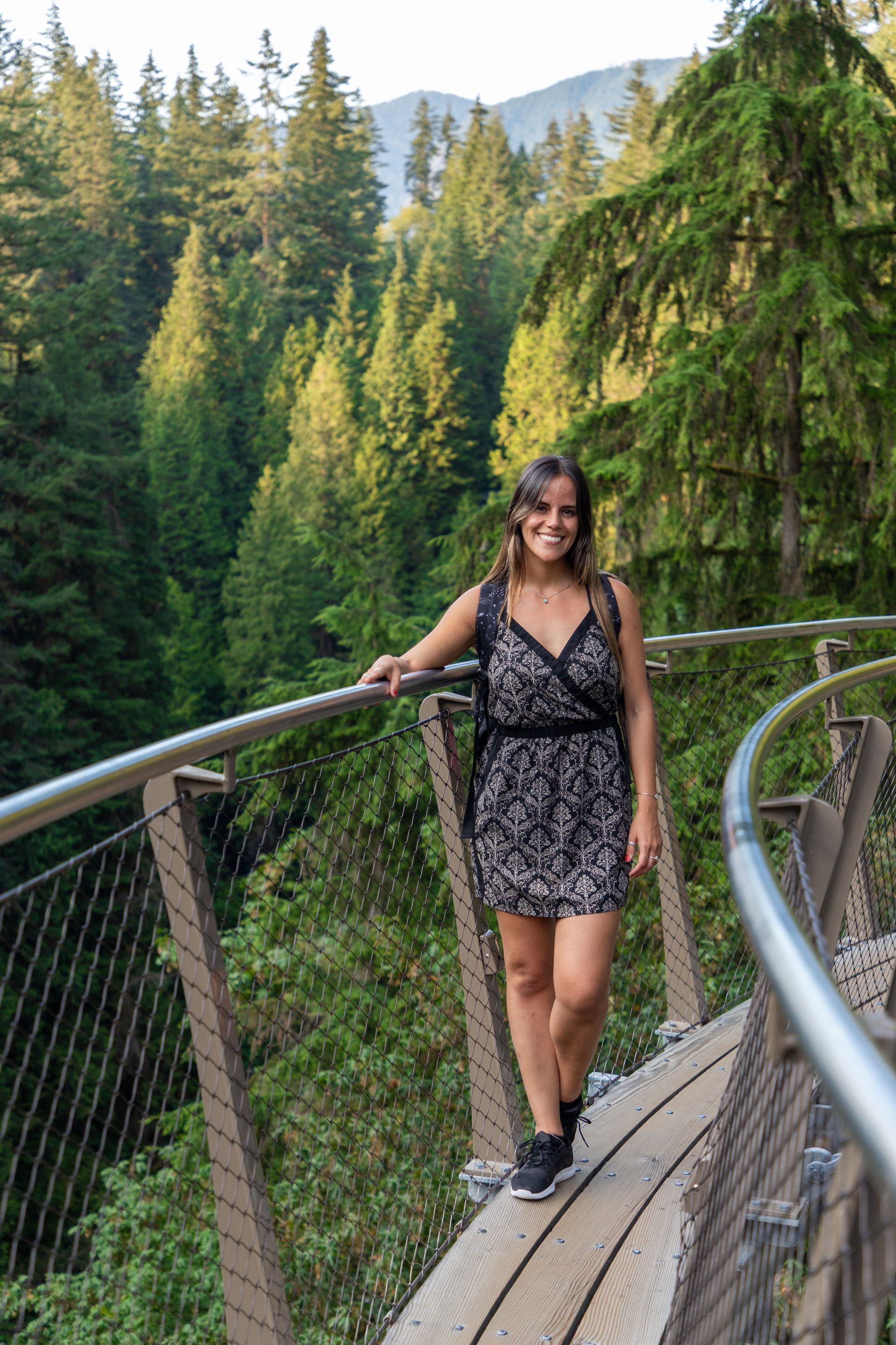 Woman standing on a forest canopy walkway with mountains and evergreen trees in the background