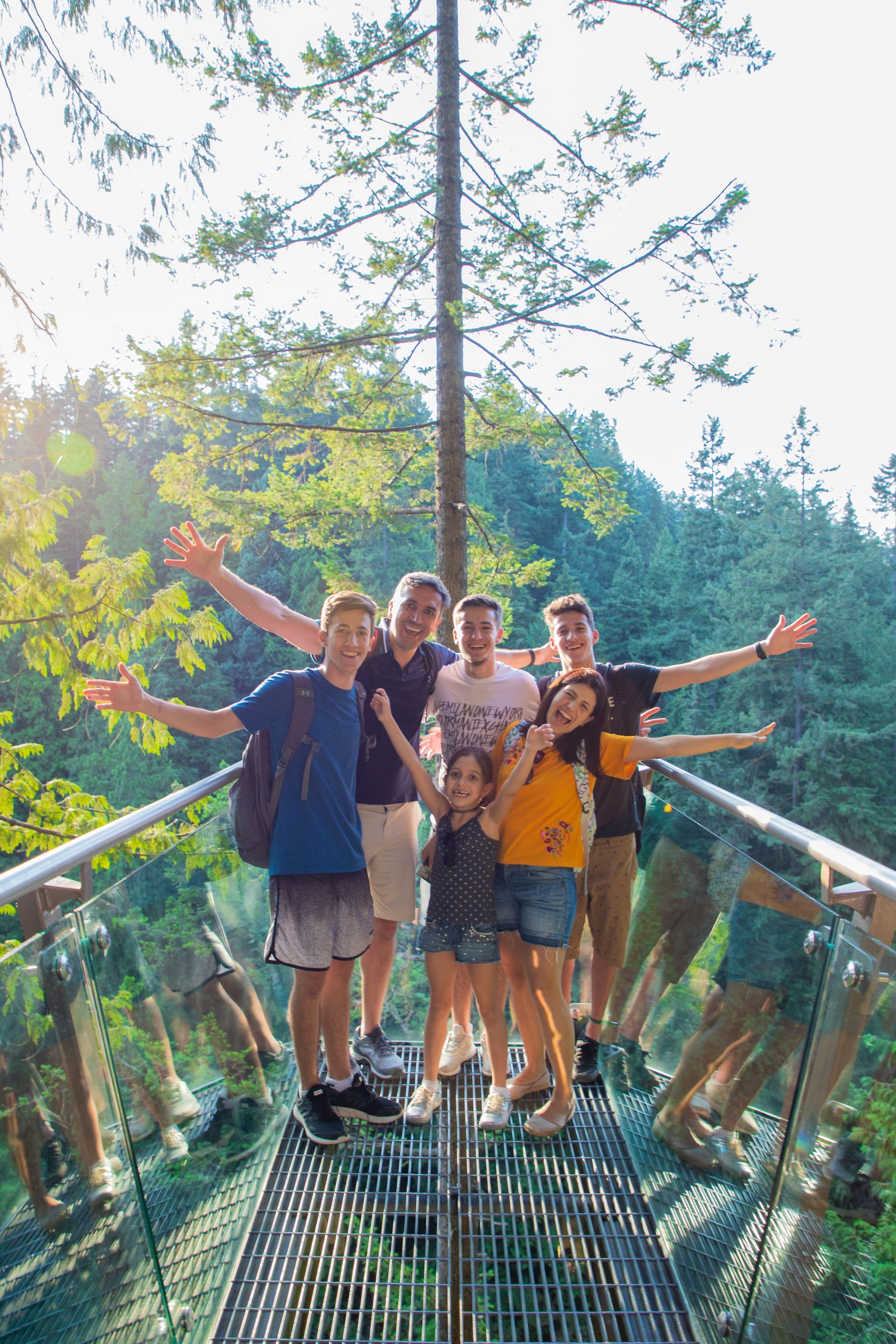 Group of hikers posing on a forest canopy walkway with arms outstretched in sunlight