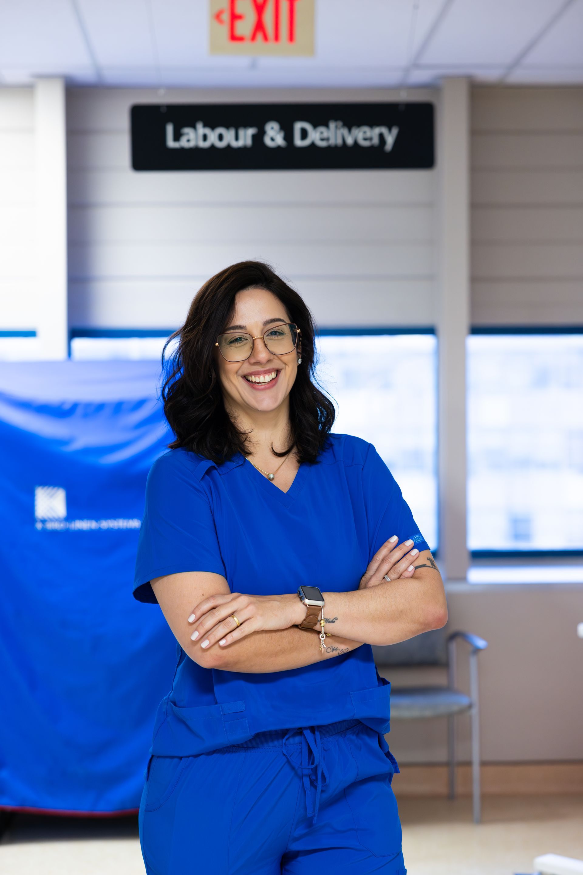 Woman in blue scrubs smiling in a hospital labor and delivery hallway.