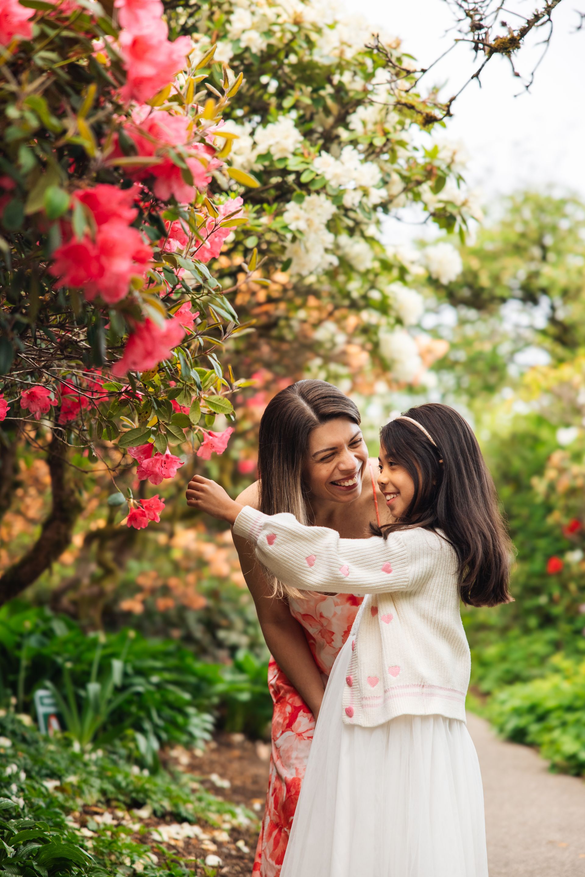 Two people smiling under blooming pink flowers on a garden path