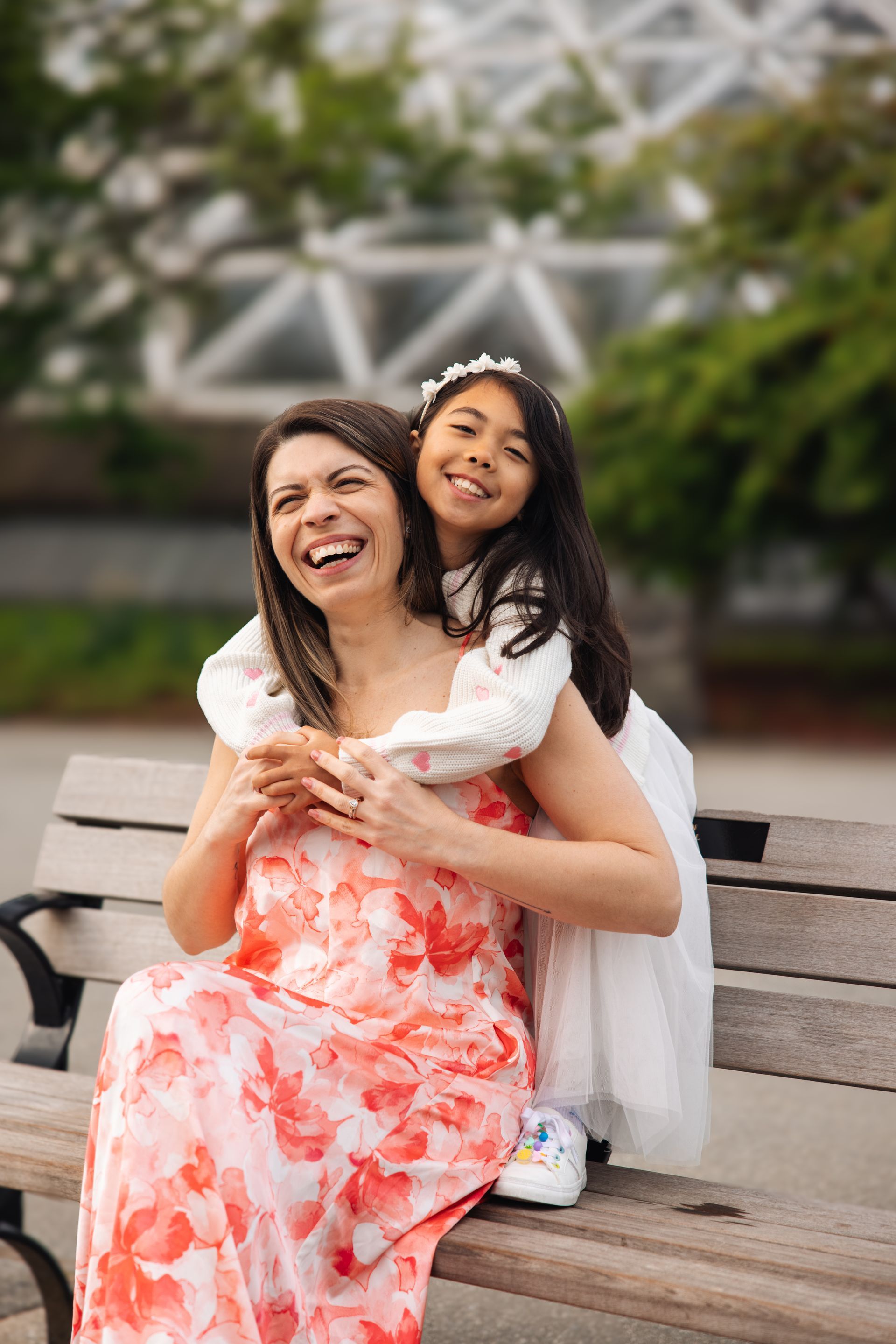 Two people smiling on a park bench, one in a white dress and one in a coral floral dress