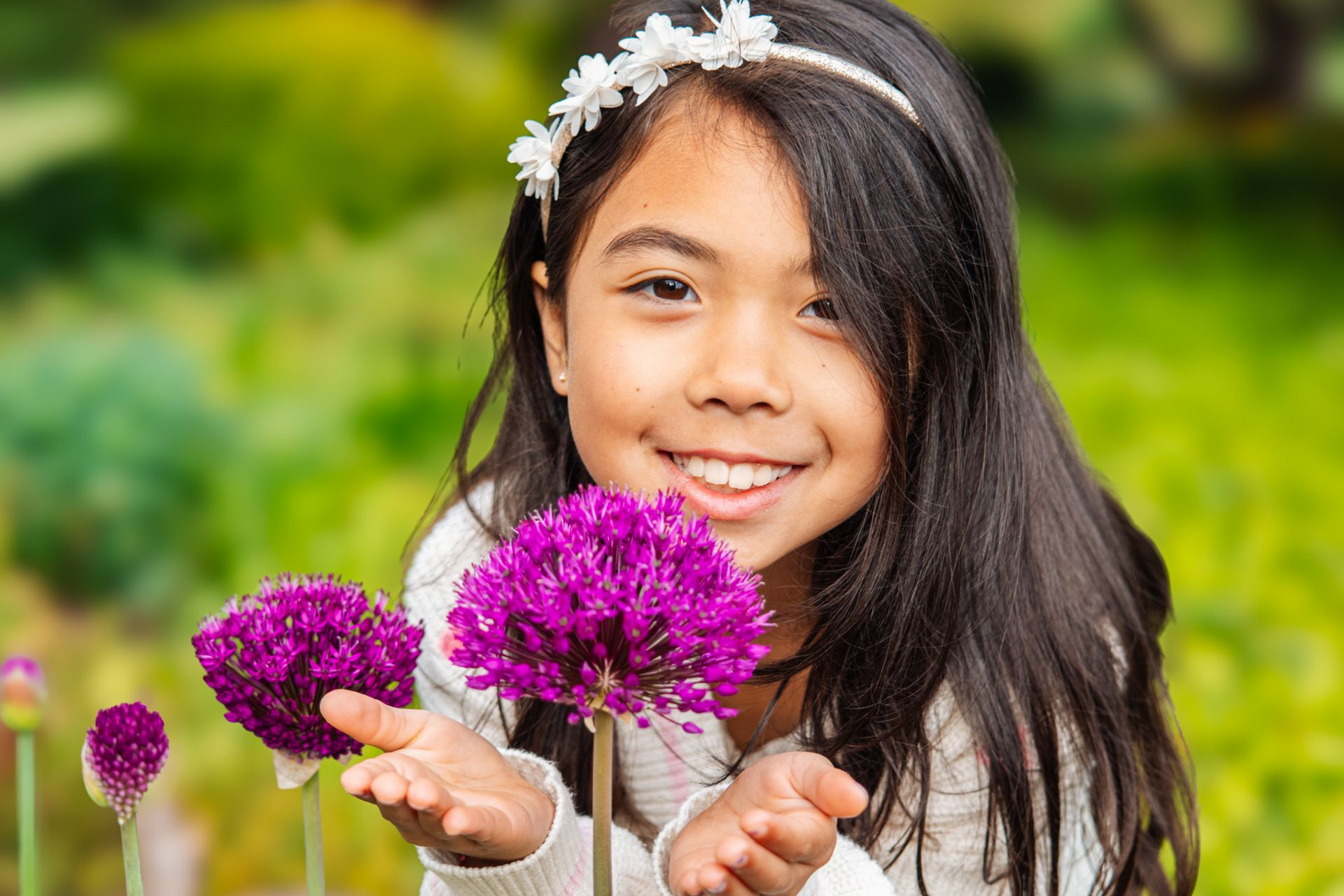 Smiling girl holding purple flowers in a green garden