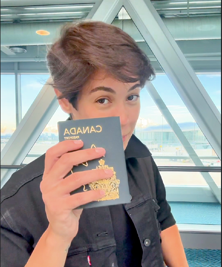 Person in a black shirt holding a card, smiling indoors near large glass windows.