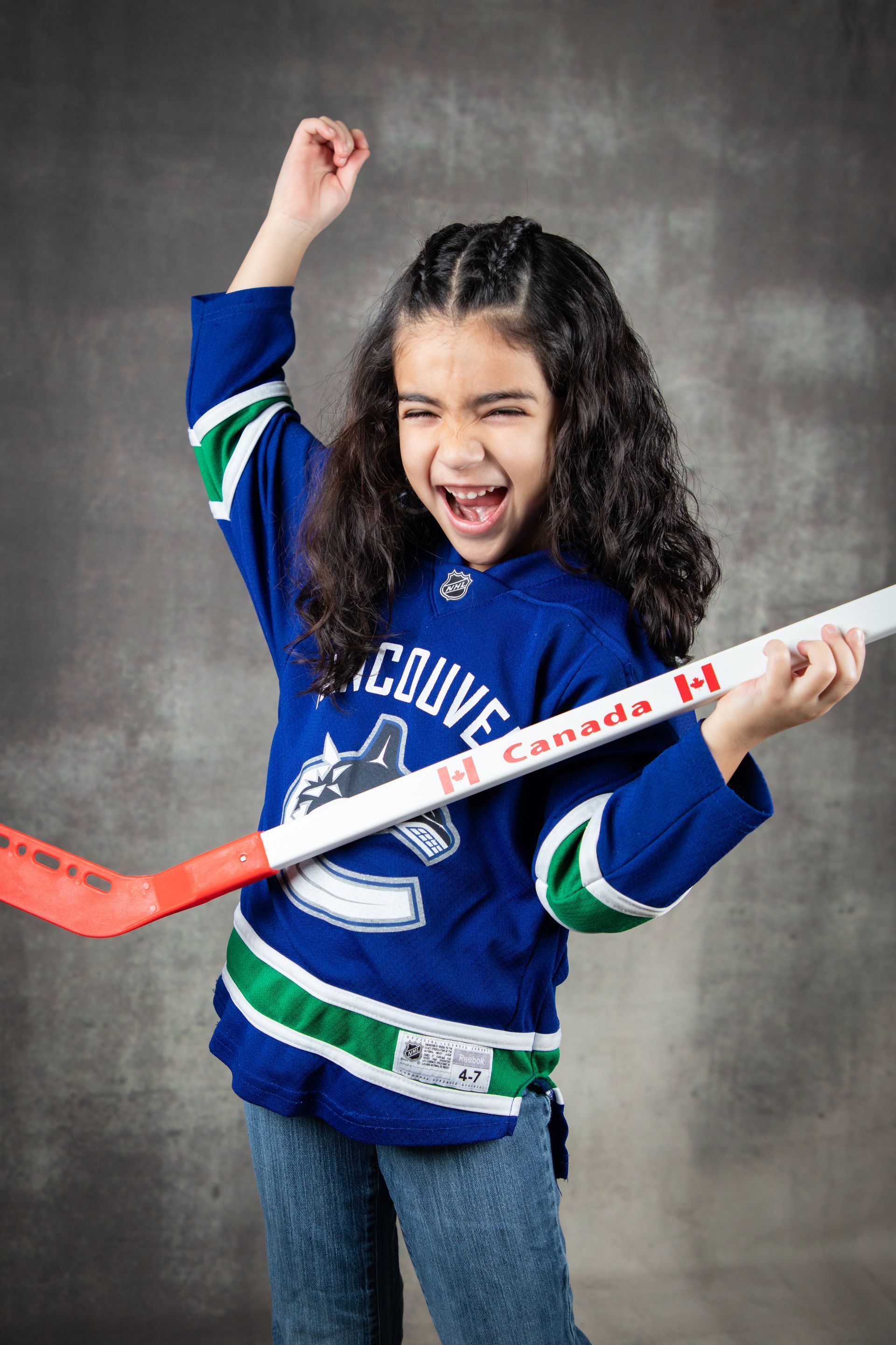 Young hockey player in a blue jersey celebrates with a raised fist and a hockey stick.