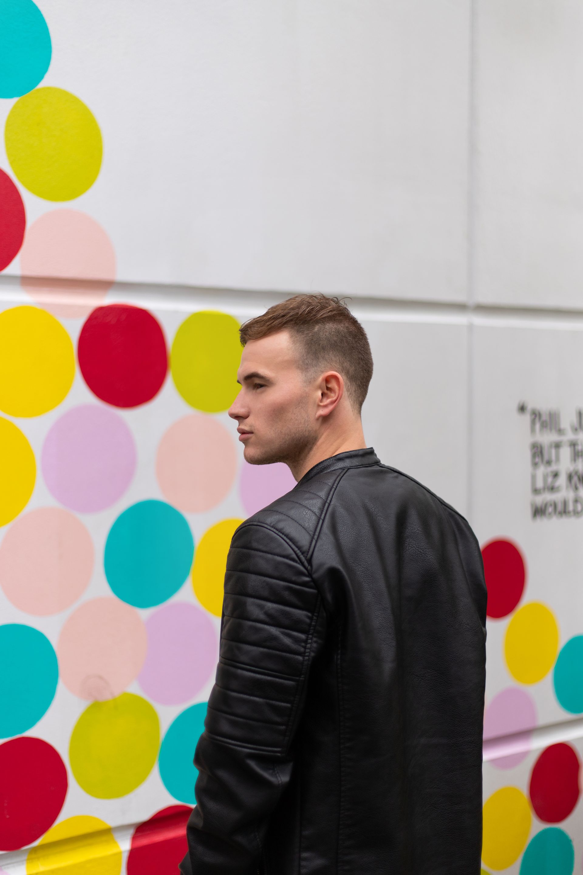 Man in black jacket standing by a wall covered with colorful polka dots