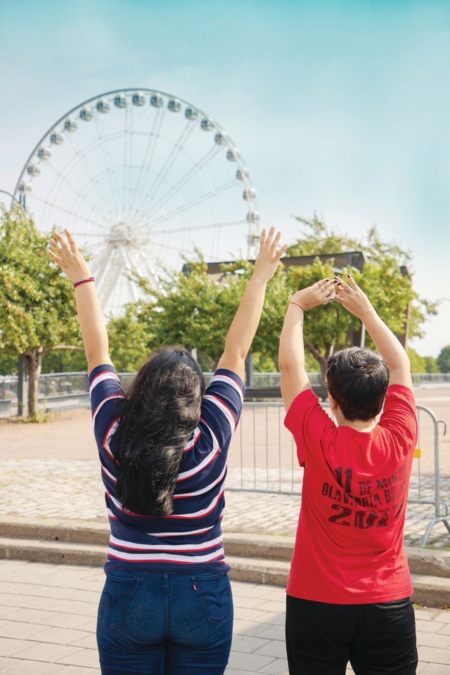 Two people raising their arms toward a Ferris wheel in a sunny park