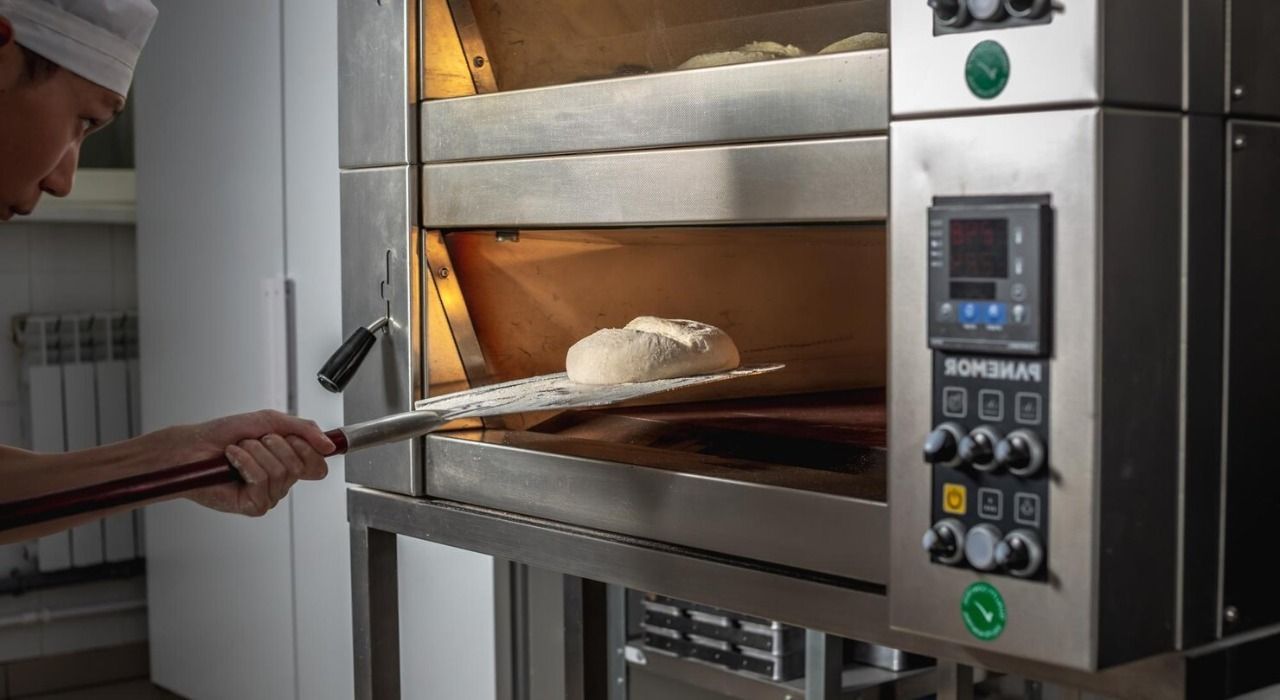 Baker slides bread into a commercial oven with a long wooden peel.