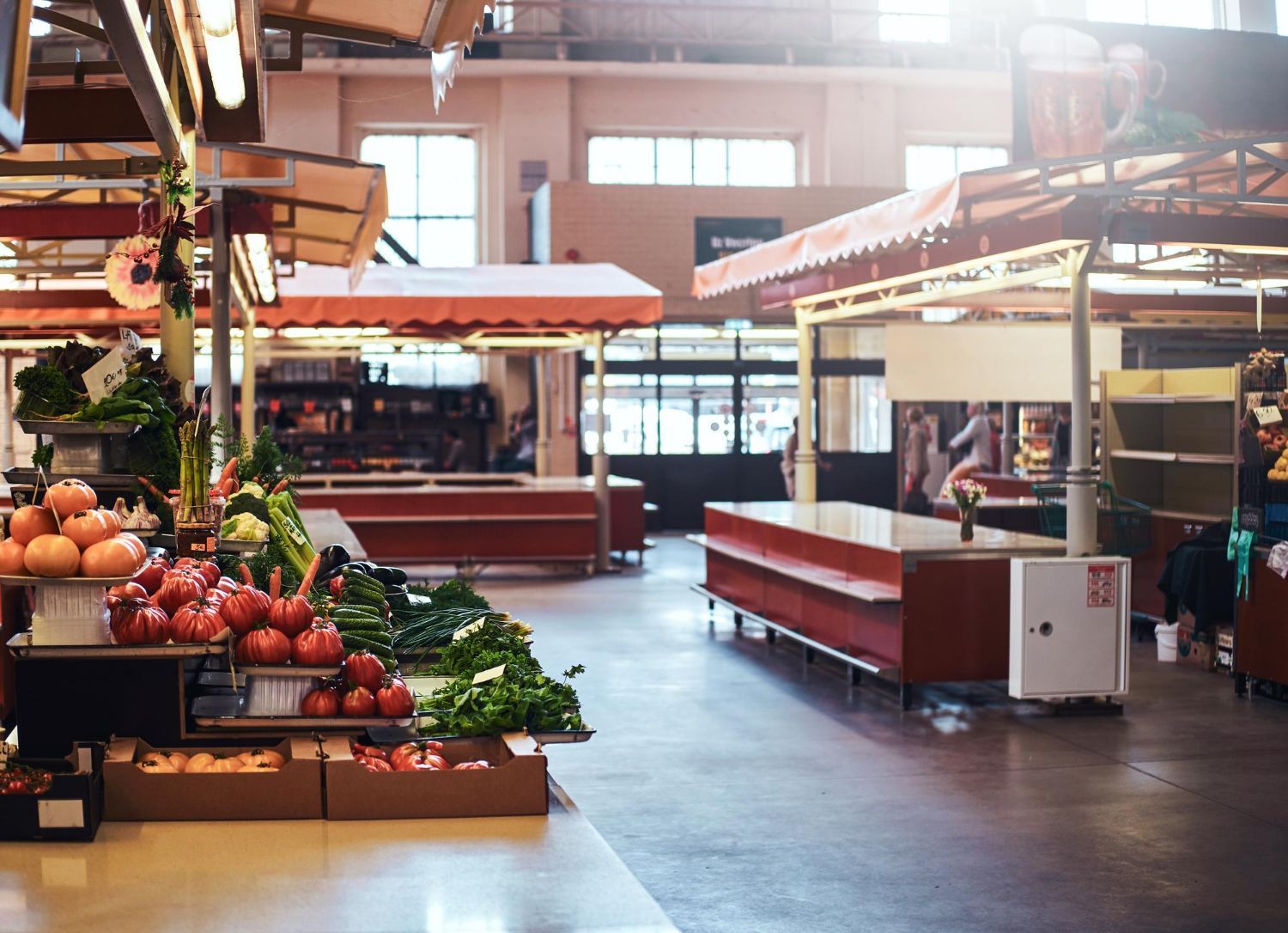 Indoor market with empty produce stalls and baskets of fruits and vegetables under bright skylights