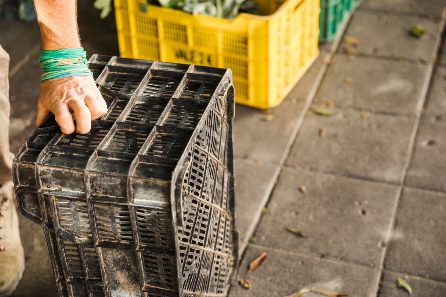 Hand carrying stacked black plastic crates beside yellow bins on a tiled floor