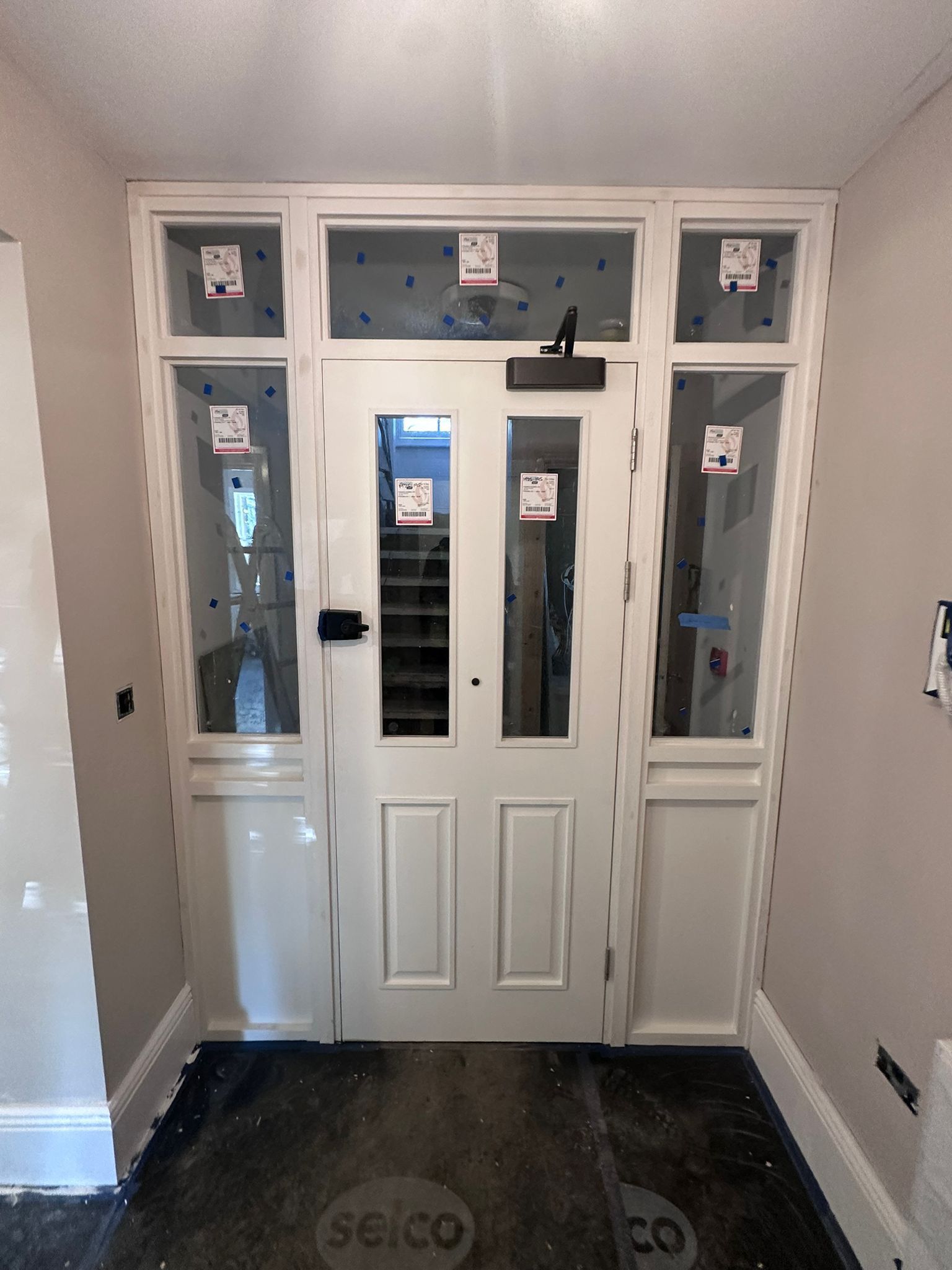 White door with glass panels and sidelights in a hallway, construction debris on floor.