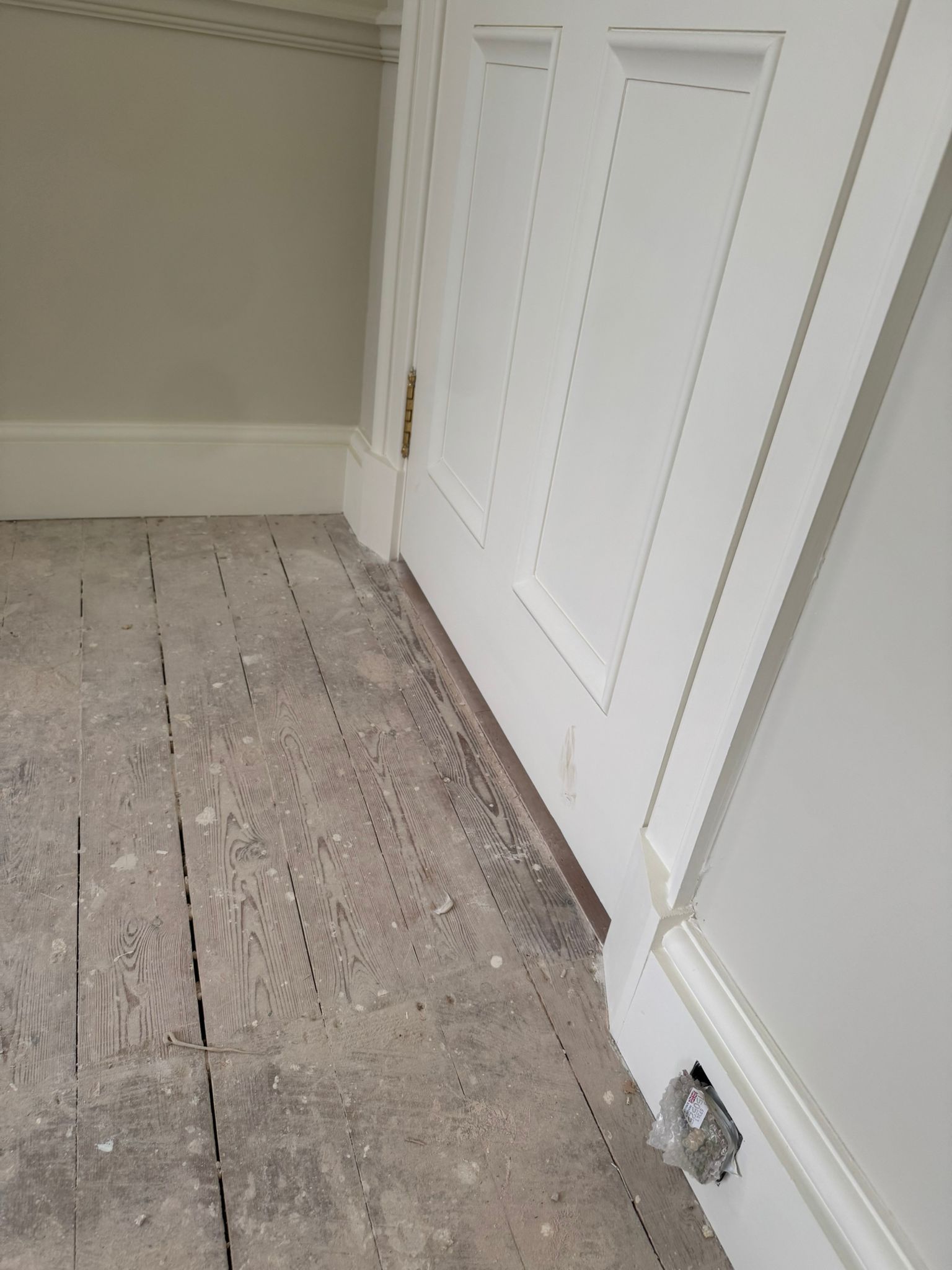 White door next to worn wood floor, light gray walls.