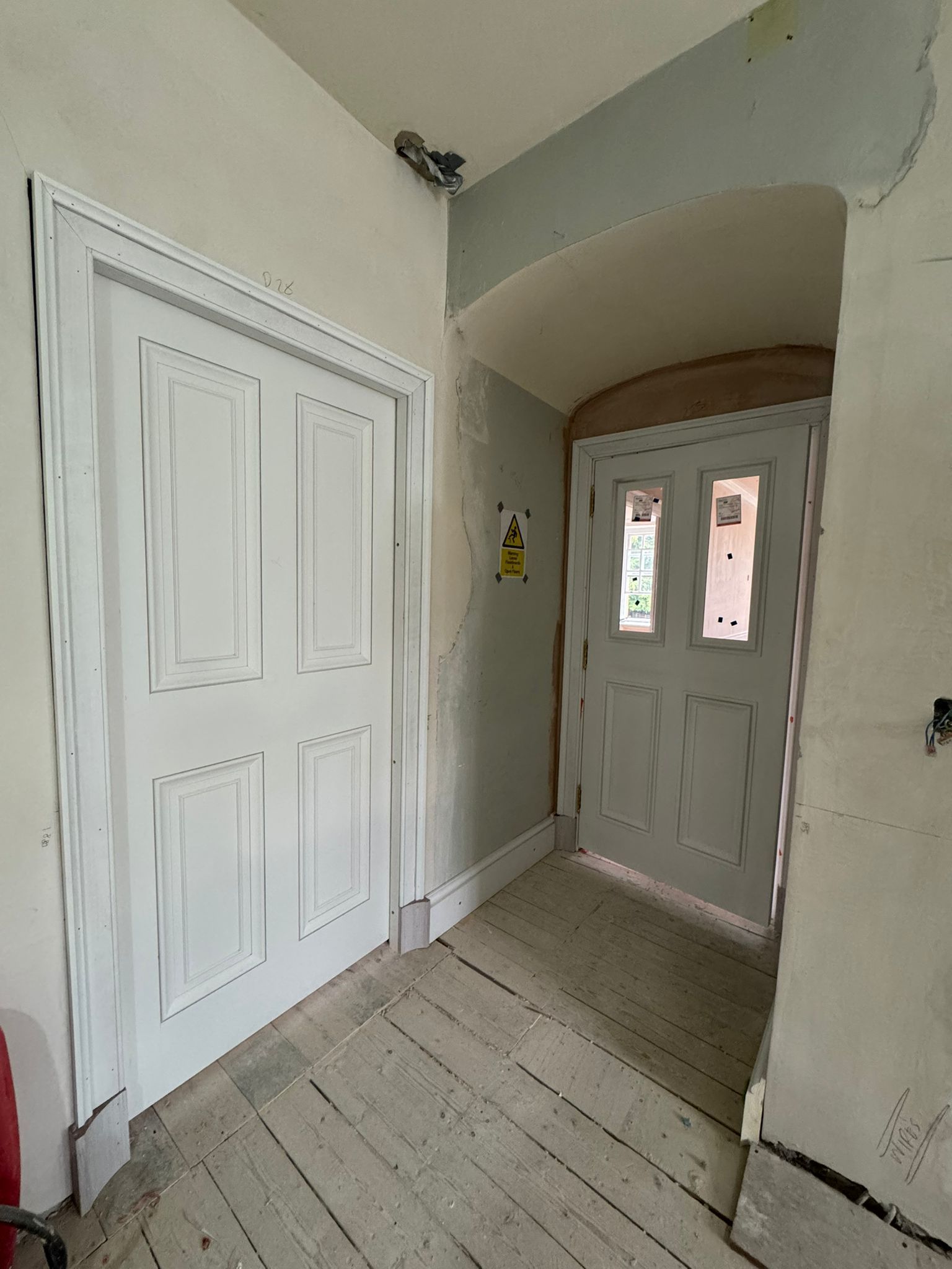 Interior hallway with two white doors, one partially open, light wooden floor, plaster walls.
