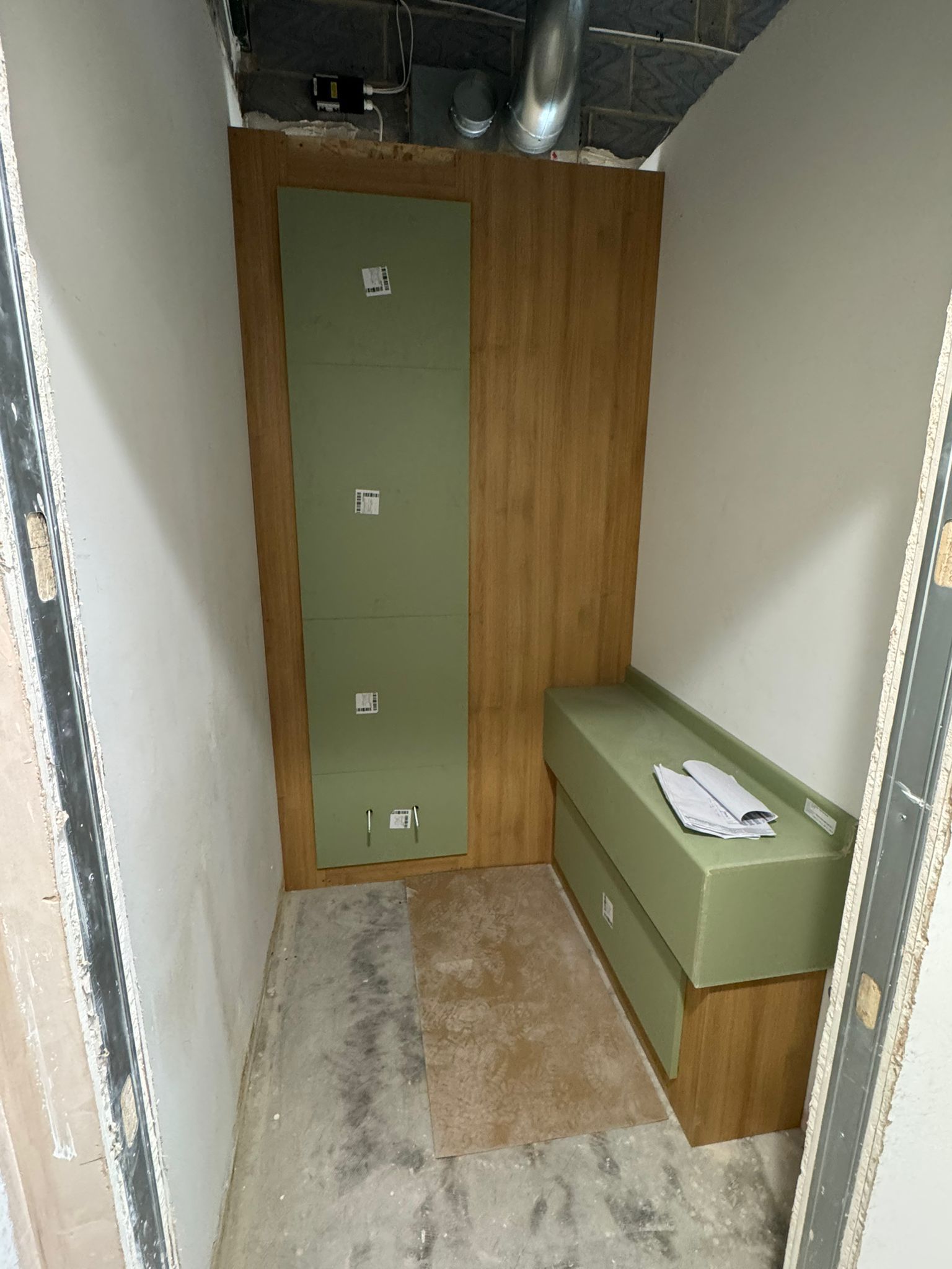 Narrow room under construction, with green and wood paneling, and a green bench.