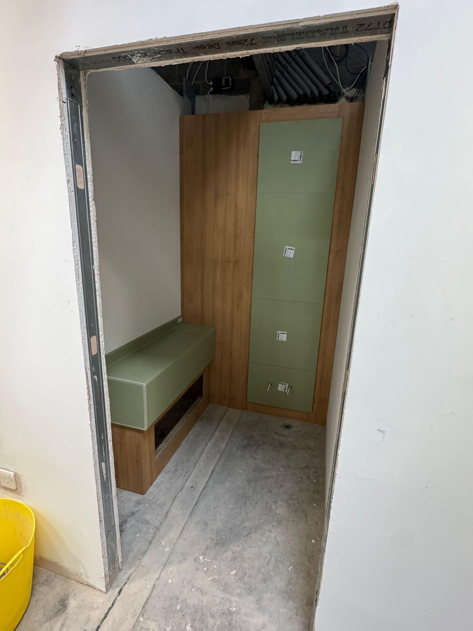 Interior of a small room under construction, with a bench, wood paneling, and green wall.