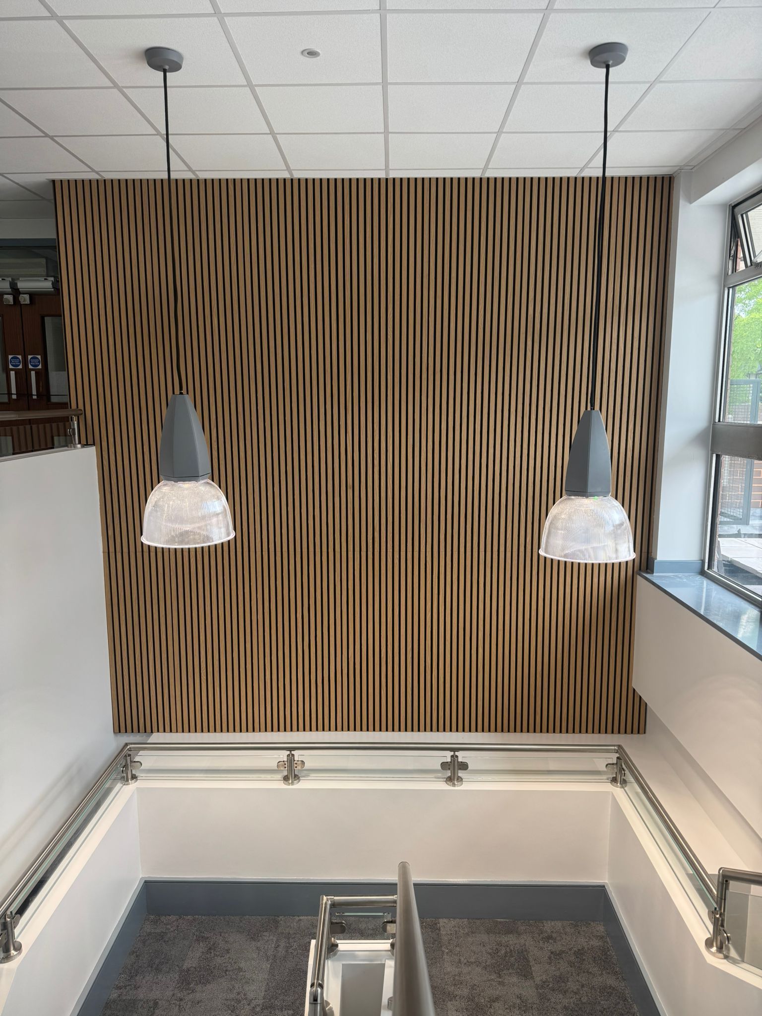 Wooden slatted wall with two pendant lights over a stairwell with metal railings.