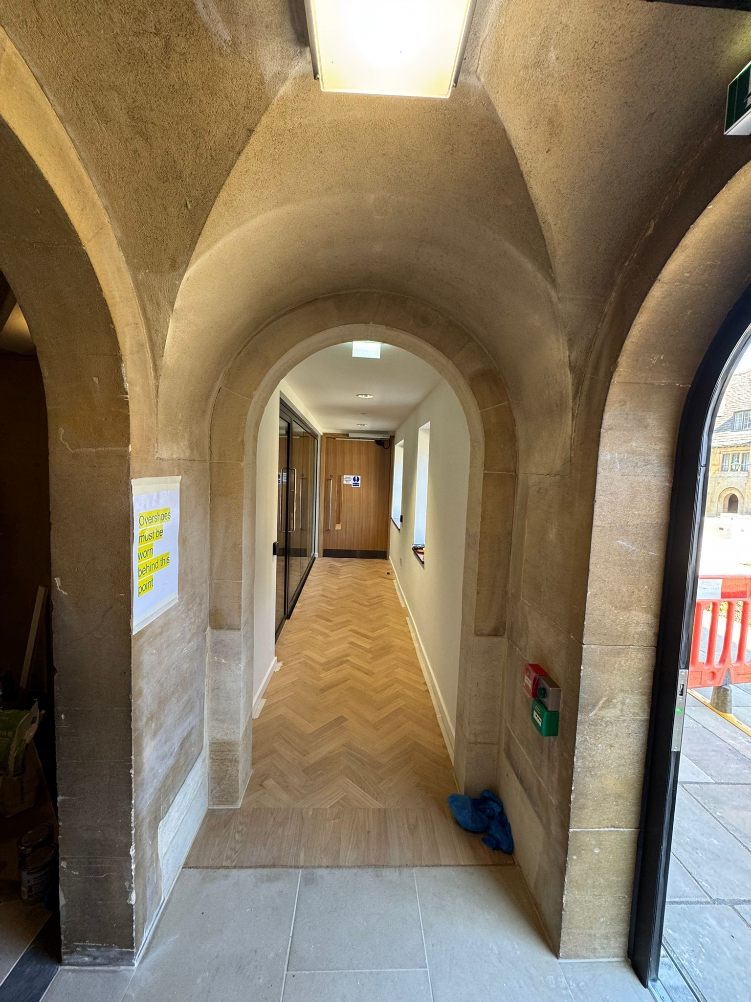Stone arched hallway with wood floor, leading to a door at the end.