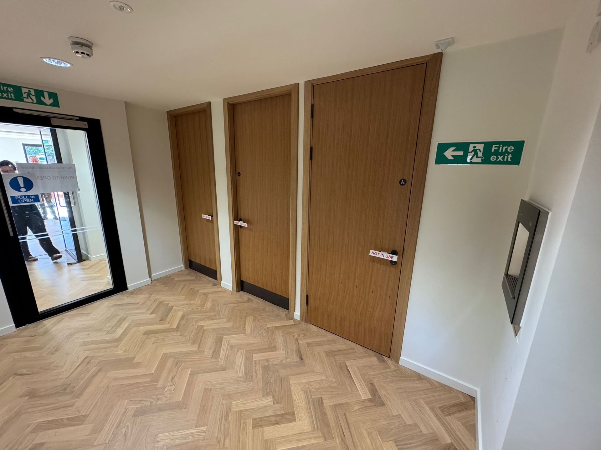 Hallway with wooden doors, herringbone floor, and an exit sign.