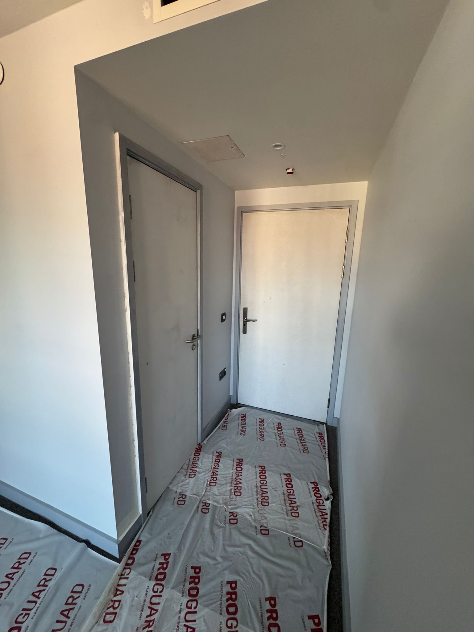 Narrow hallway with two closed white doors, covered floor.