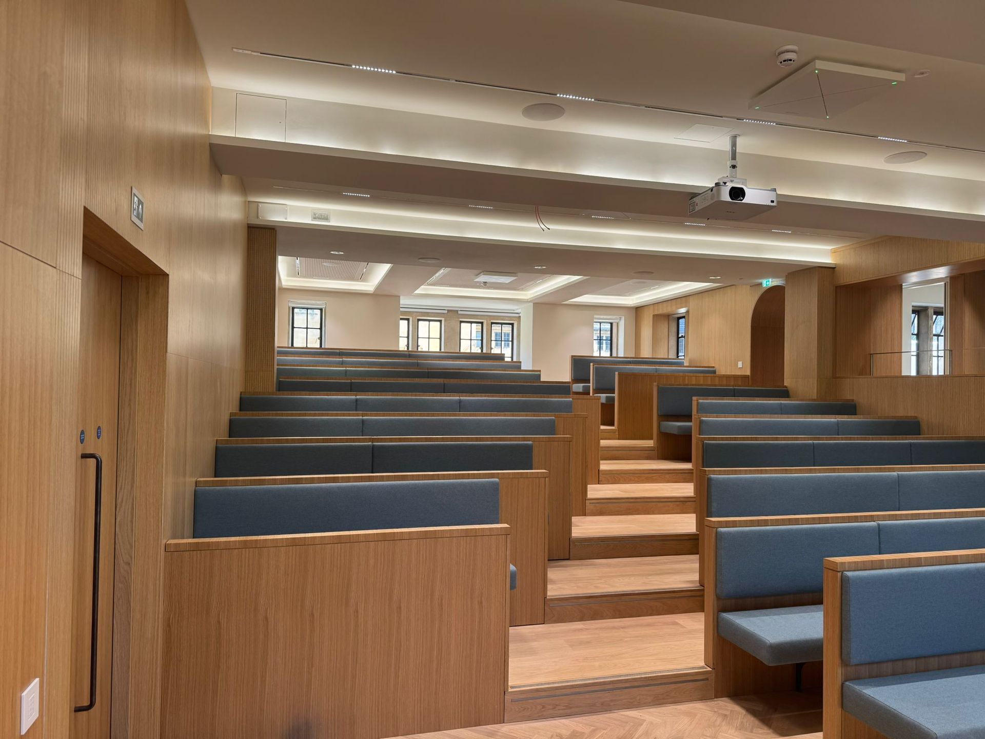 Auditorium with tiered blue seats and wood paneling. A projector hangs from the ceiling.