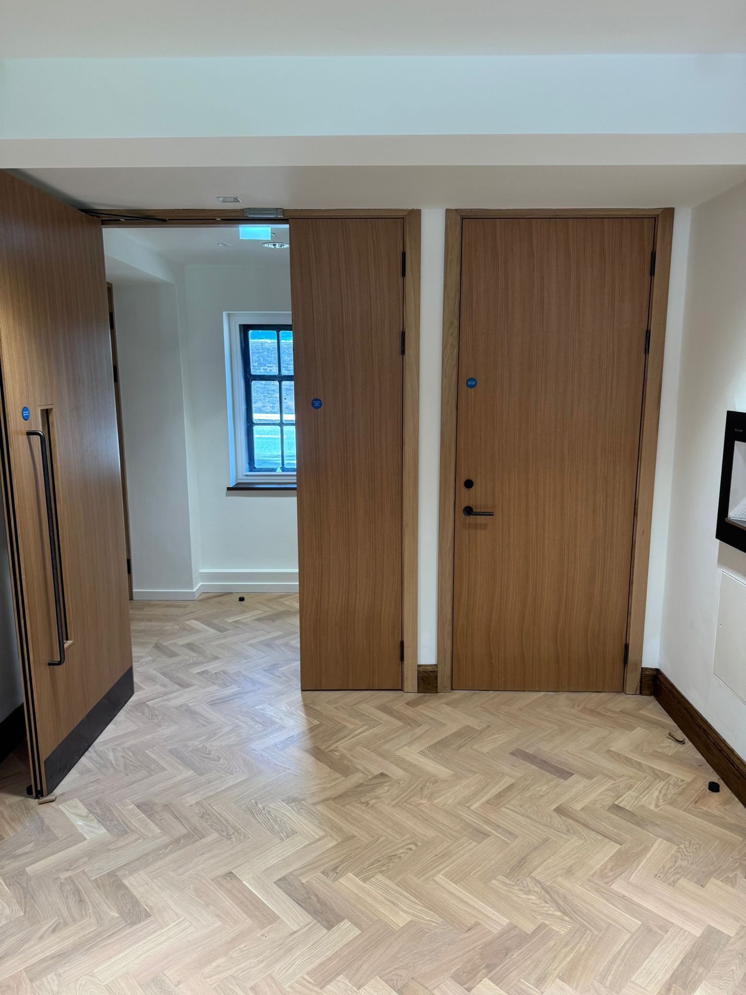 Wooden doors in hallway with parquet flooring. One door is open, showing a window.
