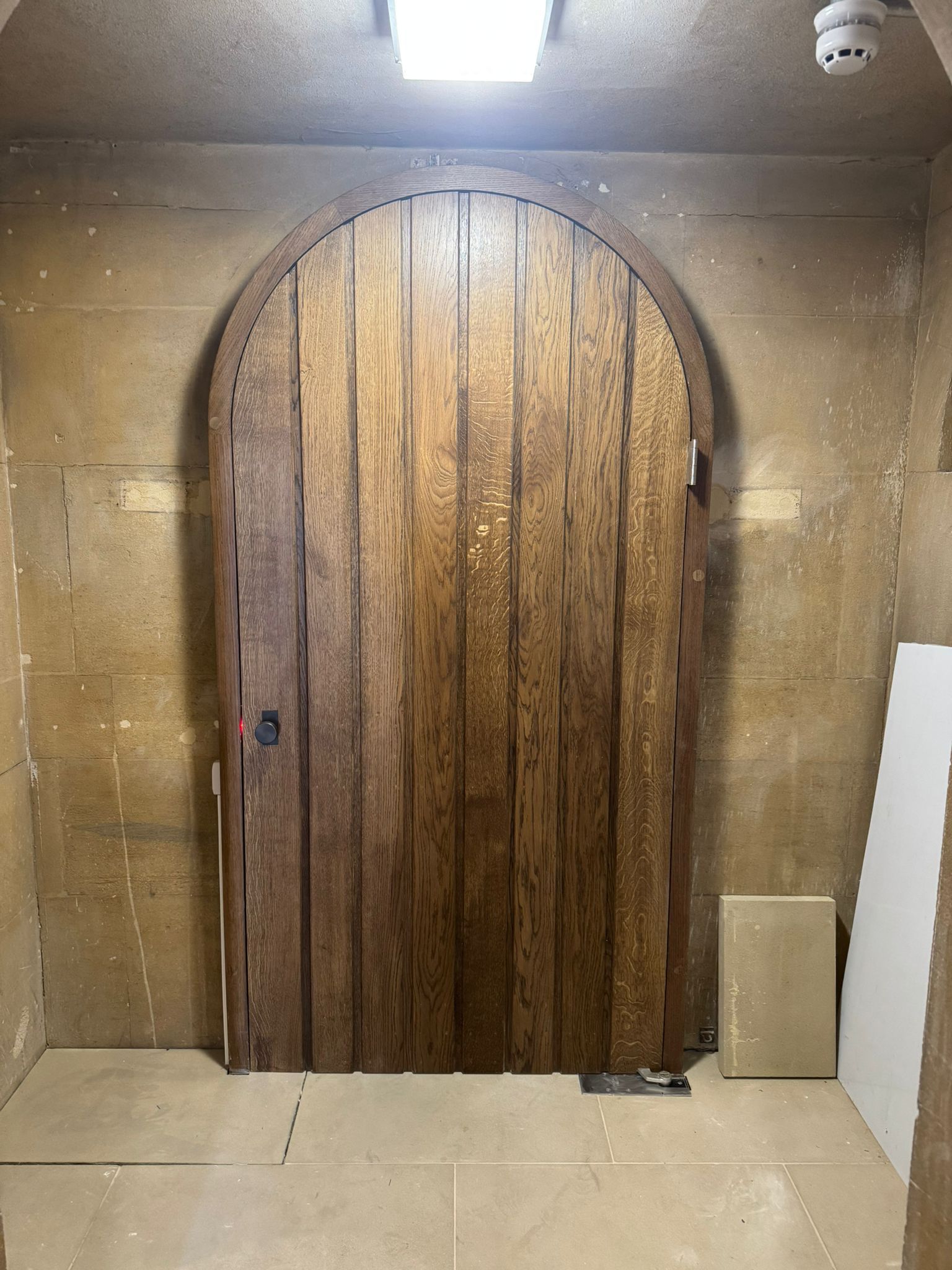 Large arched wooden door in a stone-walled room, lit from above.