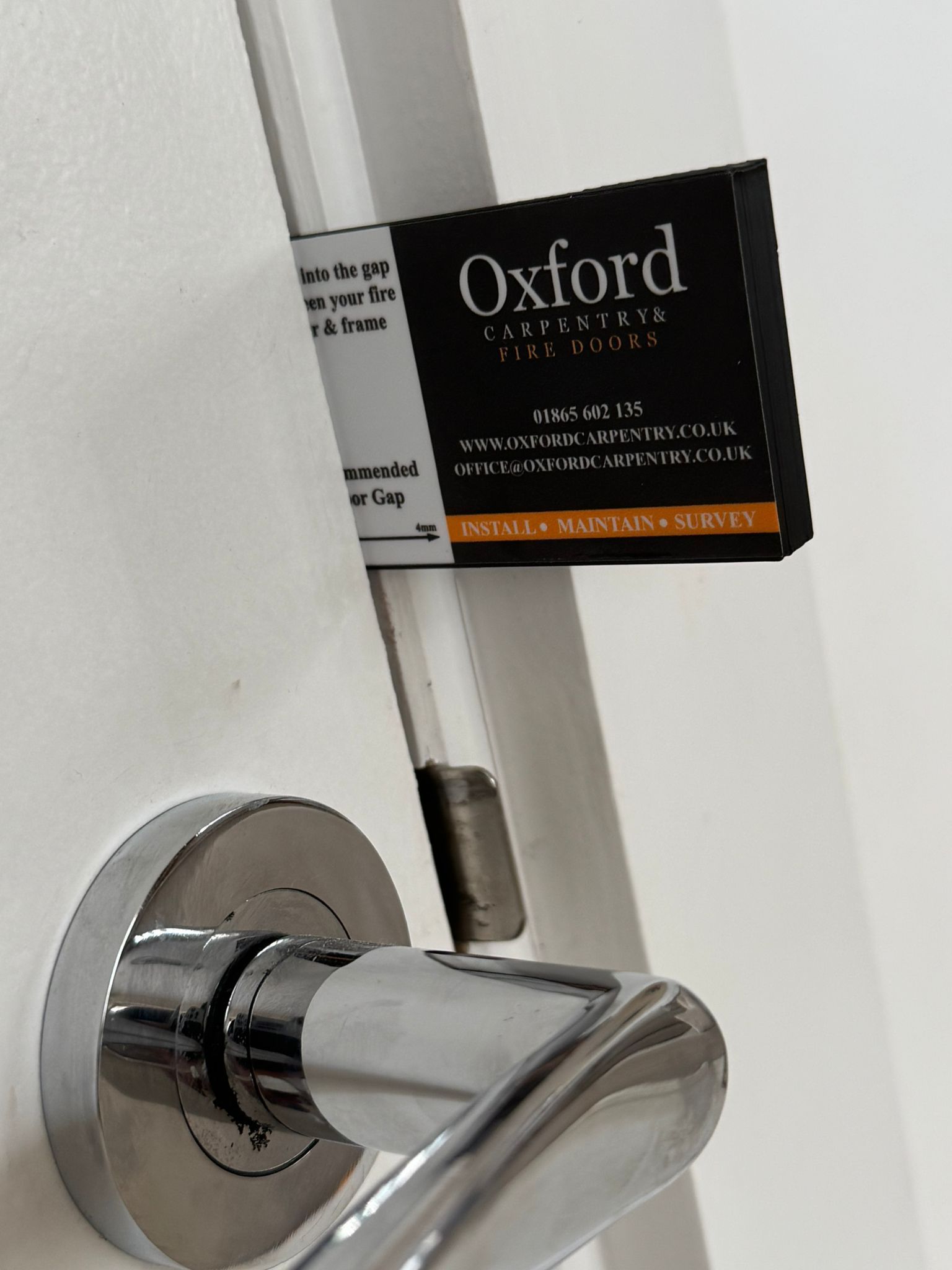 Door handle with Oxford label attached. Chrome, white door, and black/orange label.