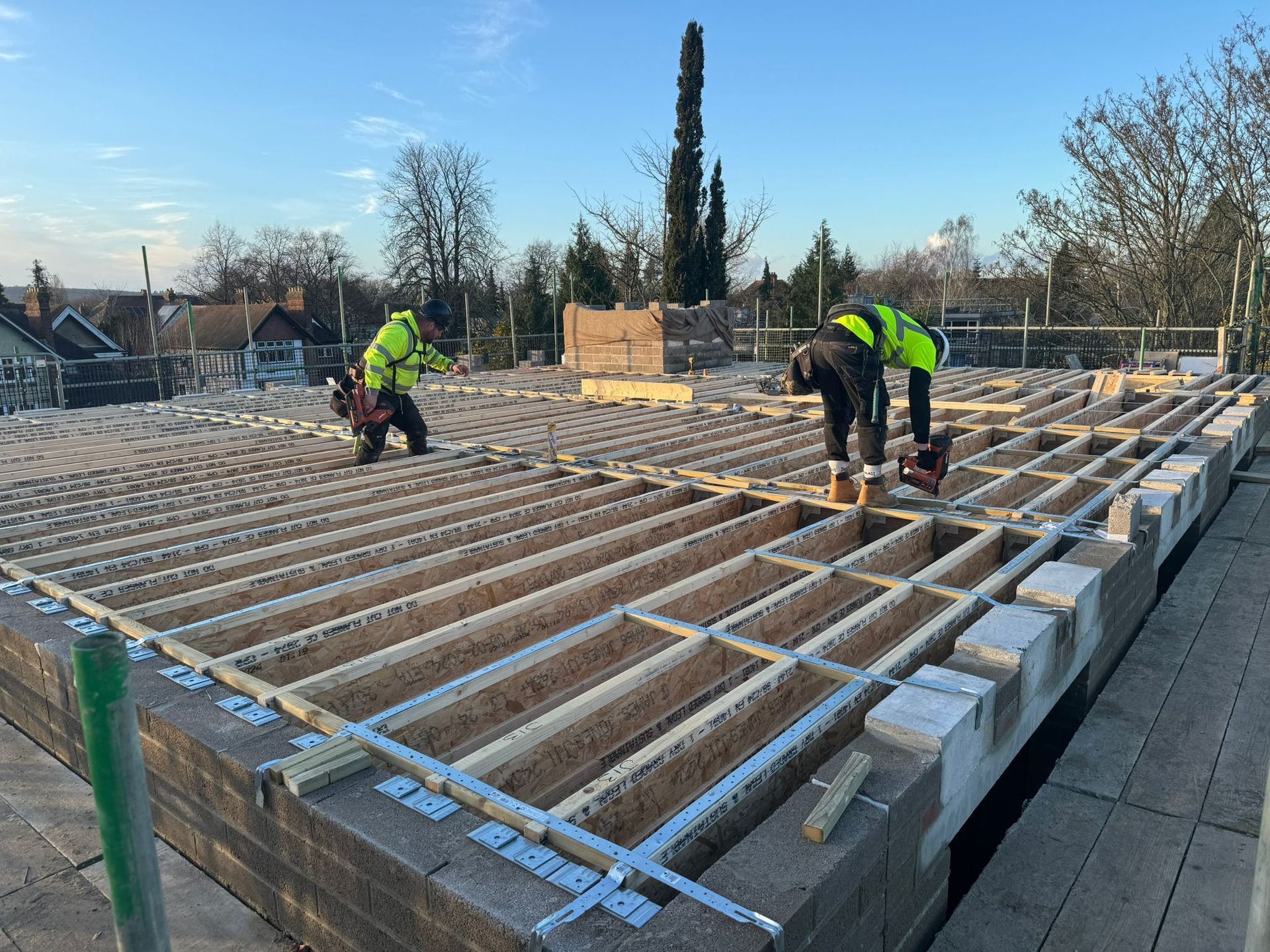 Construction workers install a wooden floor on a building rooftop, bright vests, sunny day.