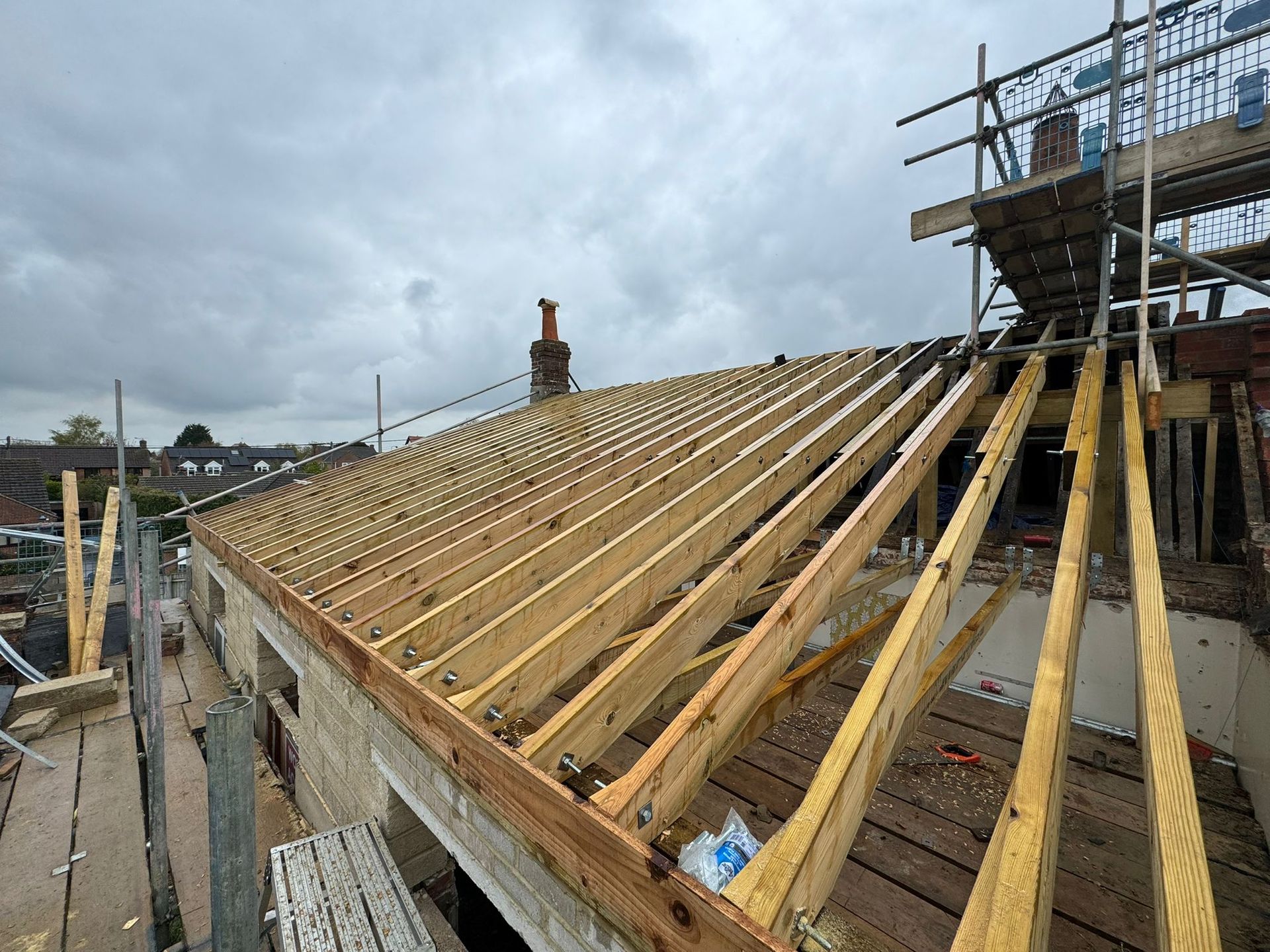 Roof construction: wooden rafters on a building with scaffolding, overcast sky.