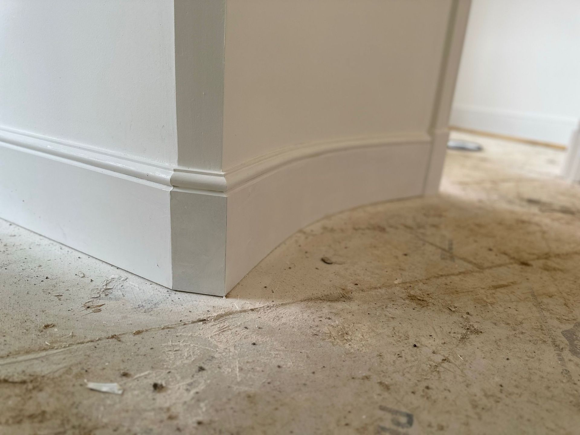 White curved baseboard corner on dusty floor.