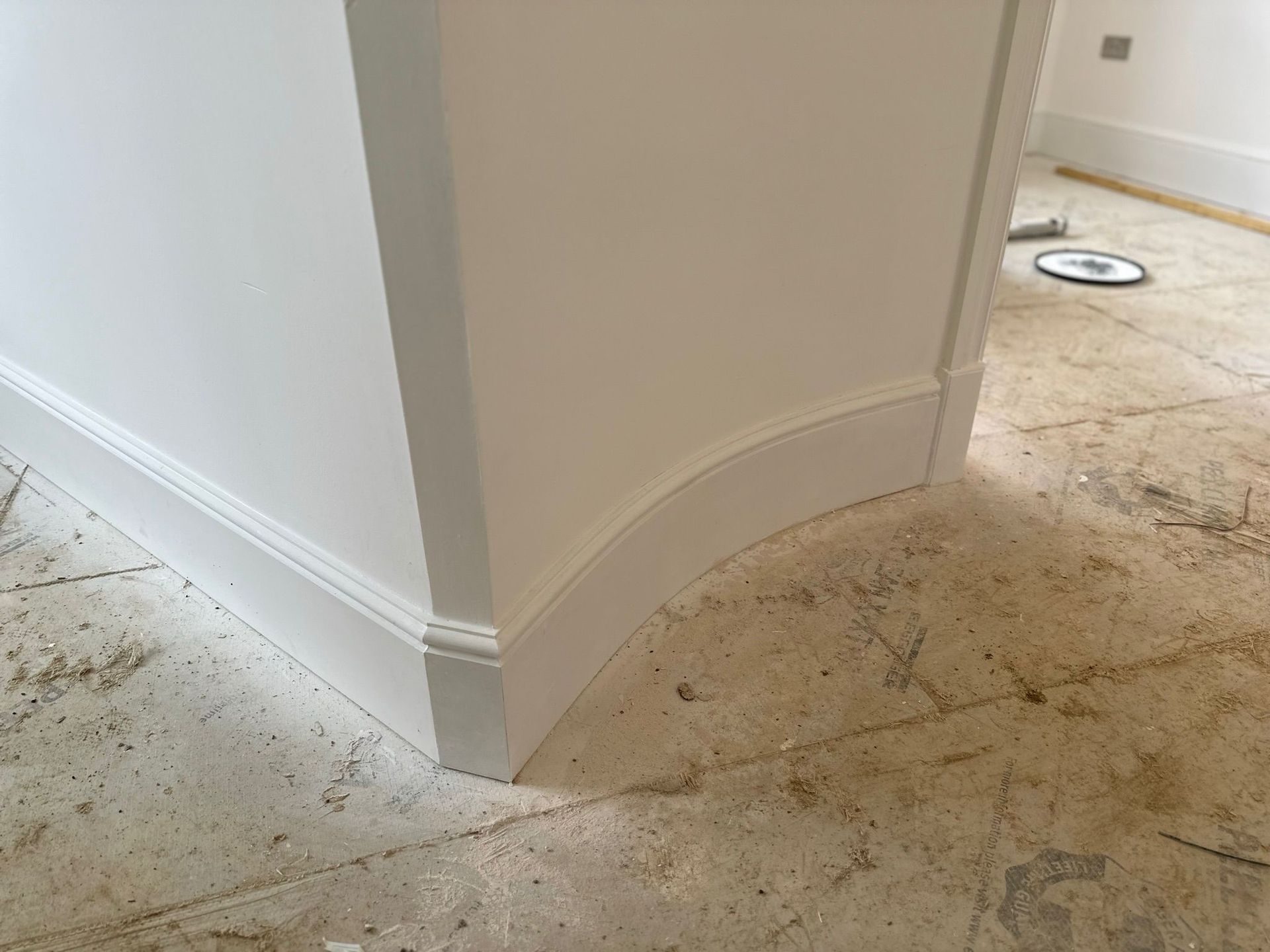 White painted wall corner with curved baseboard, unfinished flooring.