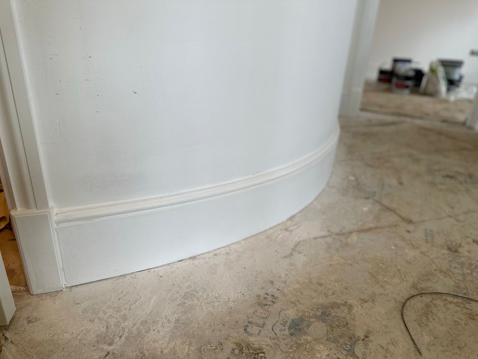 White curved wall with matching curved baseboard, unfinished floor.