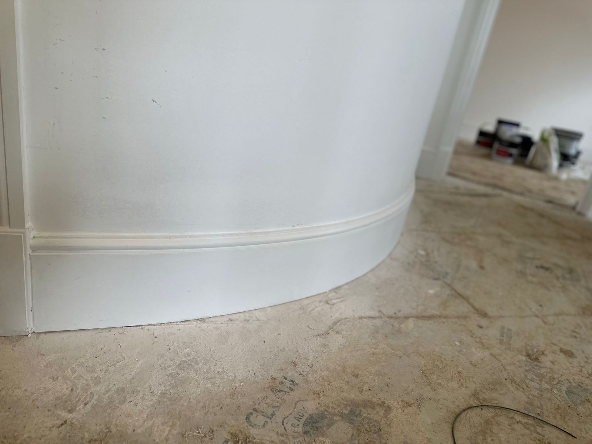 White curved wall with molding at the base, concrete floor, paint cans in background.