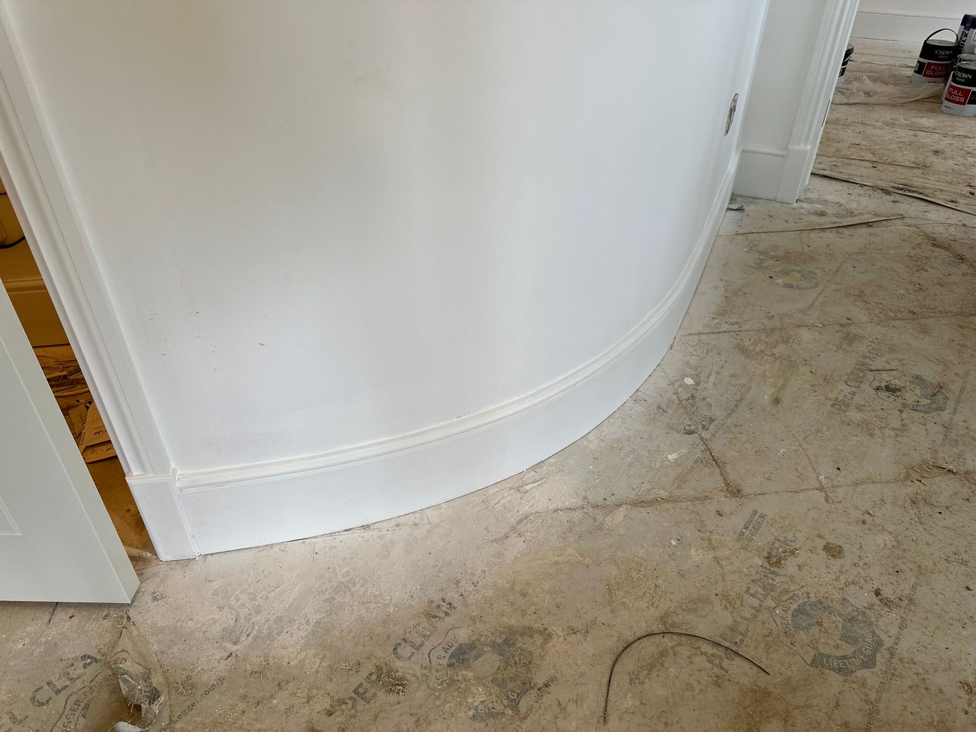 White curved wall with molding, next to an open door, and unfinished concrete floor.