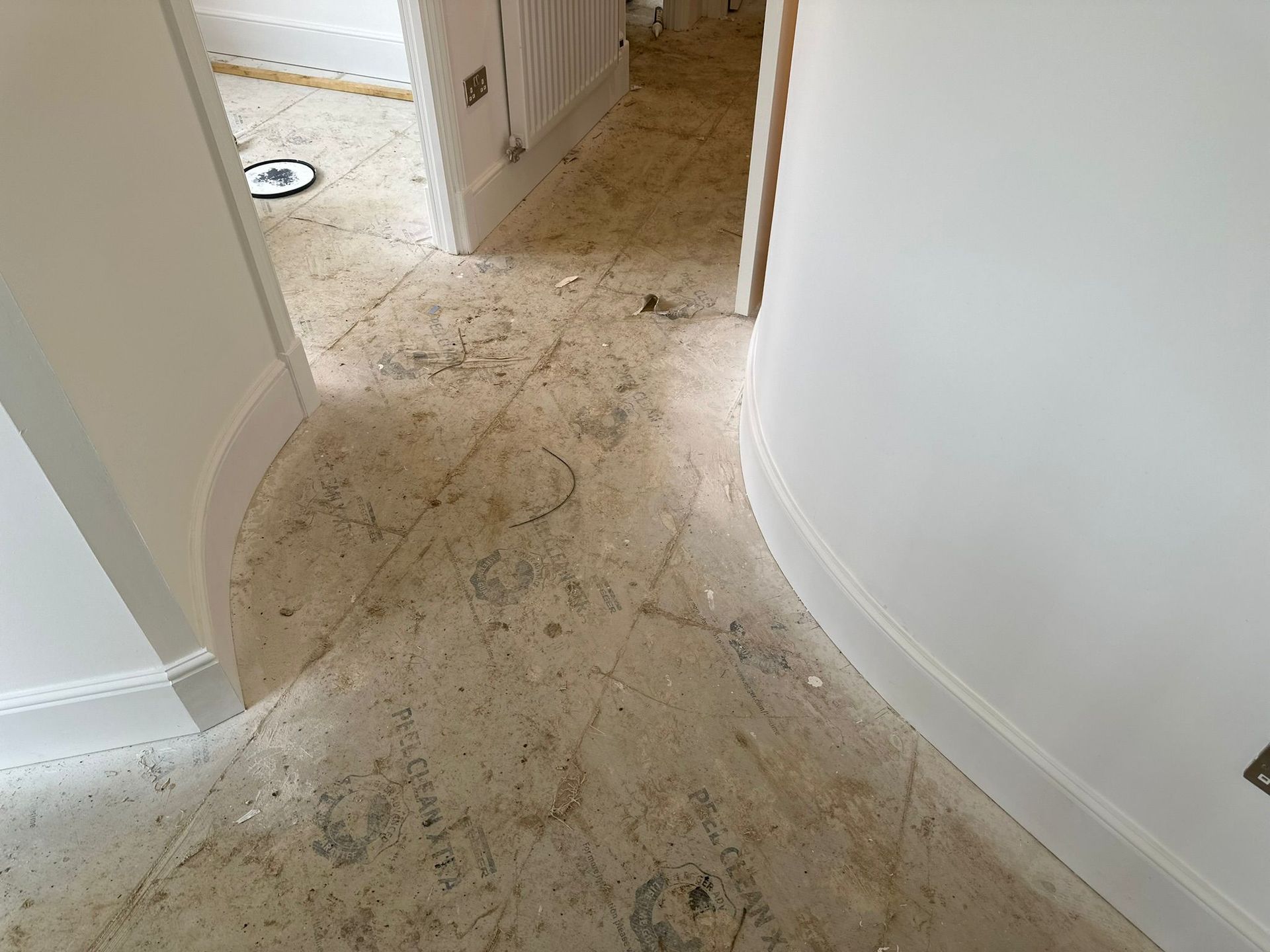Hallway with damaged floor, white walls and trim, doorway in background.