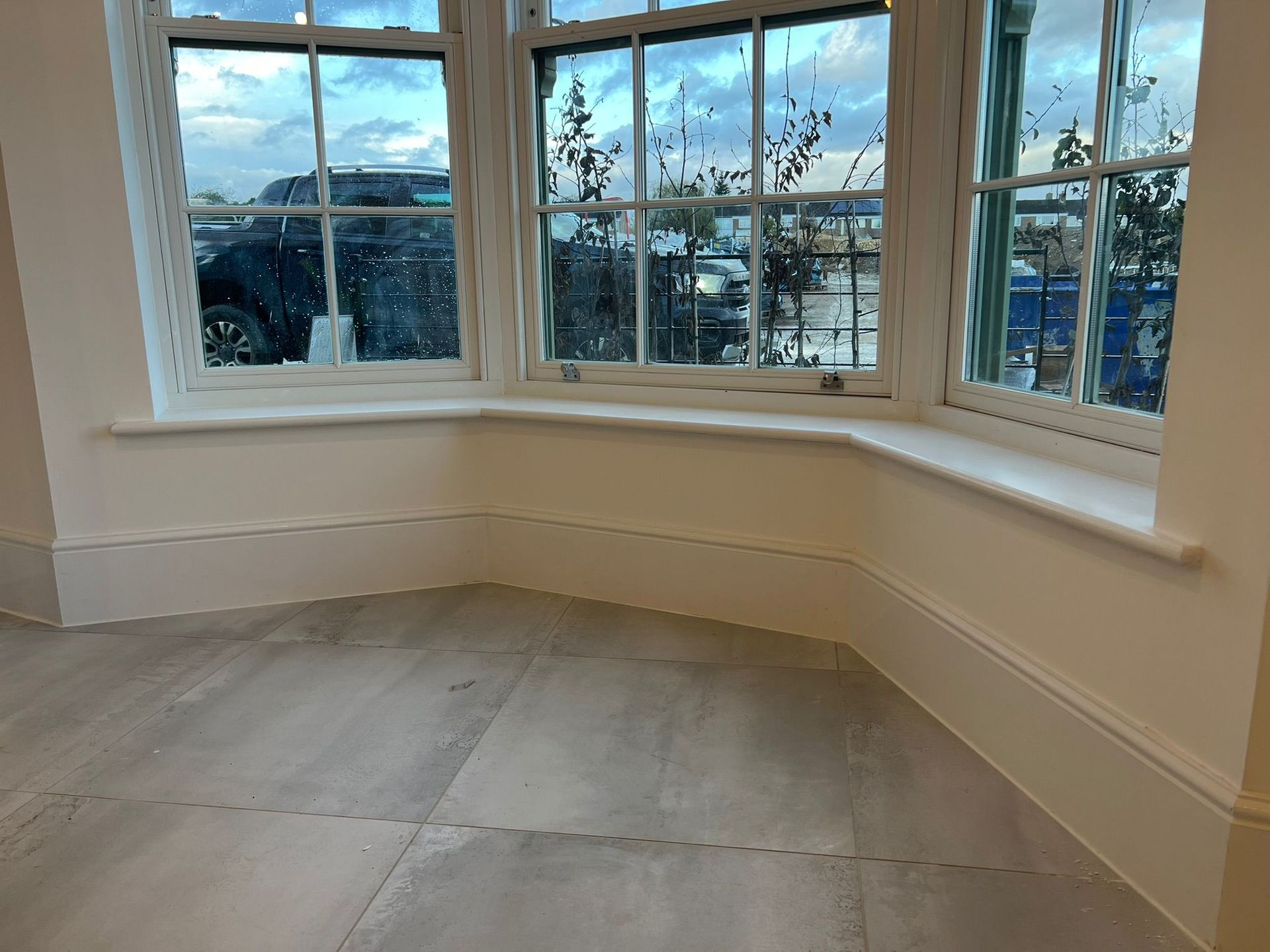 Bay window with white trim, overlooking a street scene. Light-colored flooring and walls.