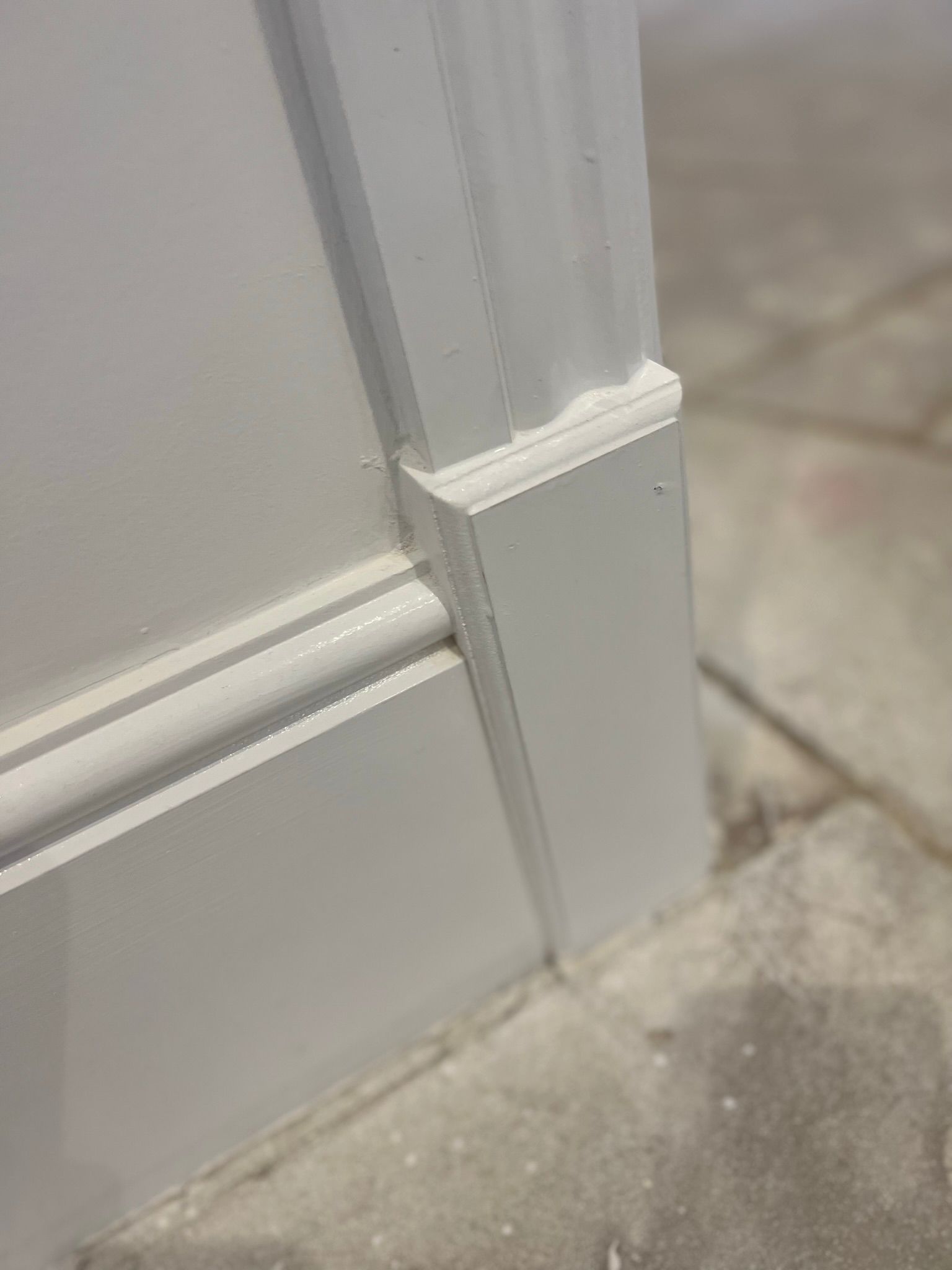 White door trim with a decorative corner, set against a gray, textured floor.