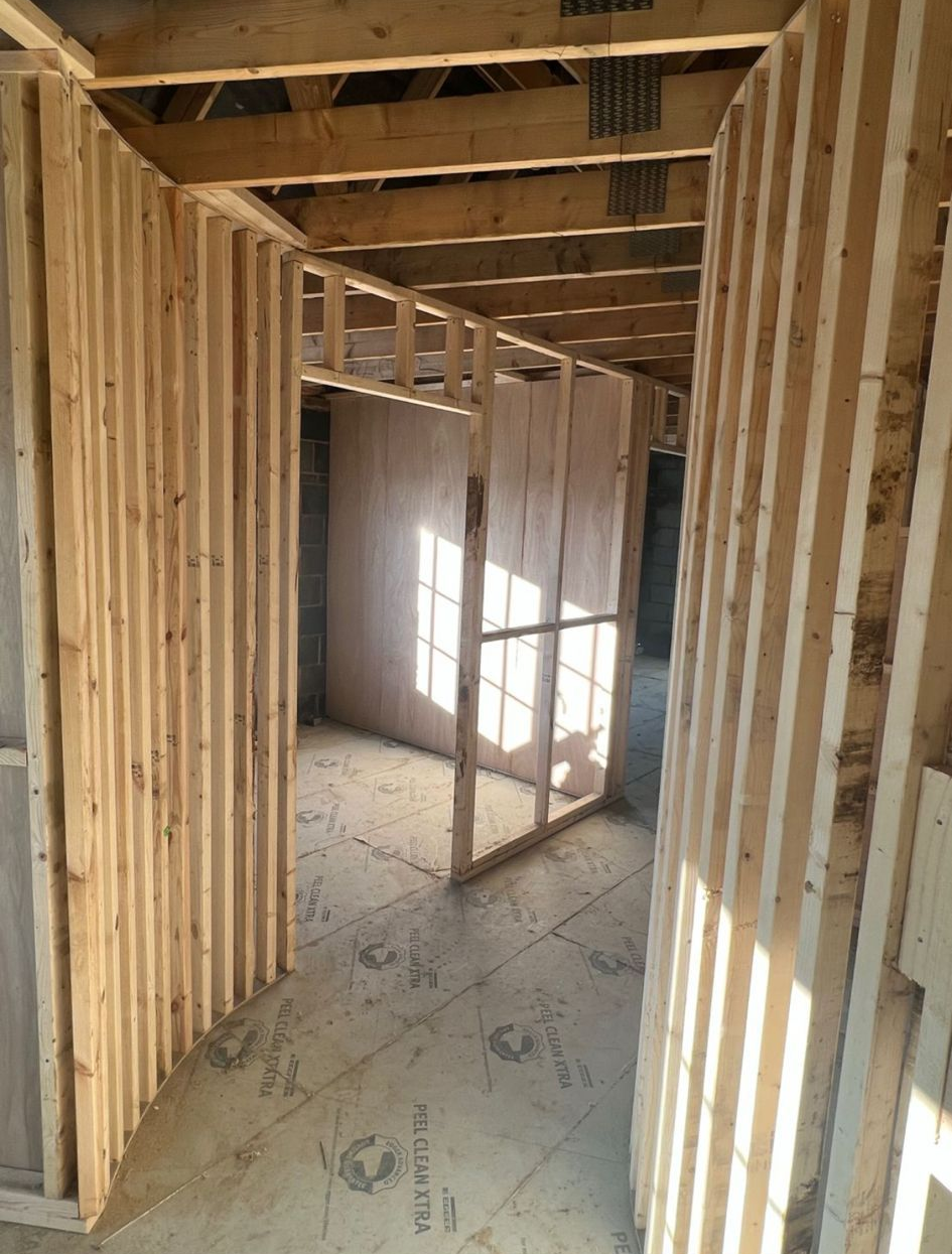Interior view of a room under construction with exposed wooden framing and partial walls.