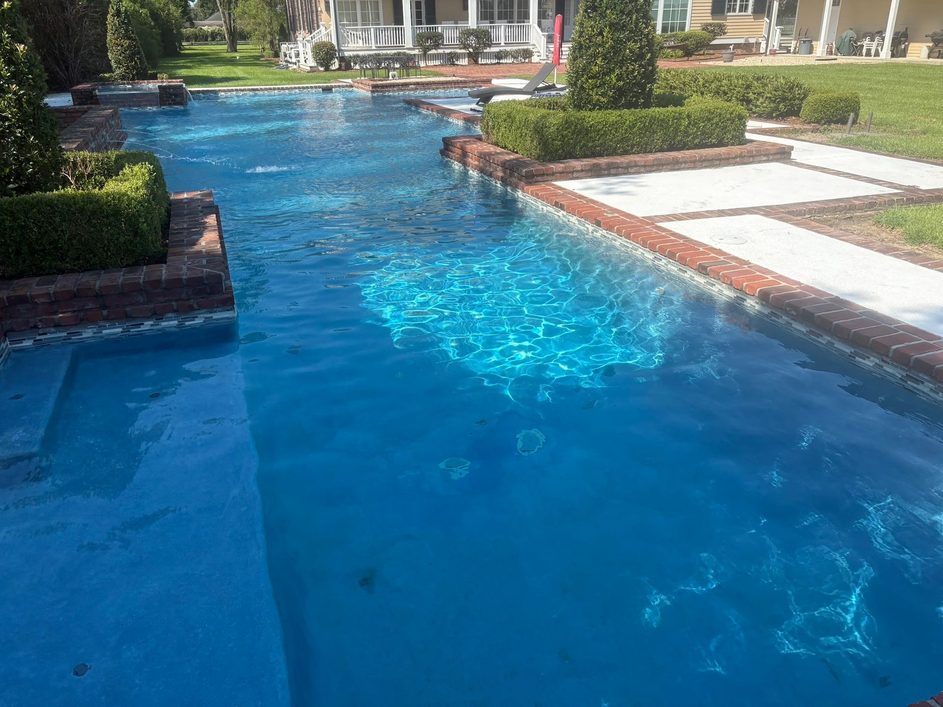 Blue swimming pool with brick edging and green hedges in a grassy backyard.