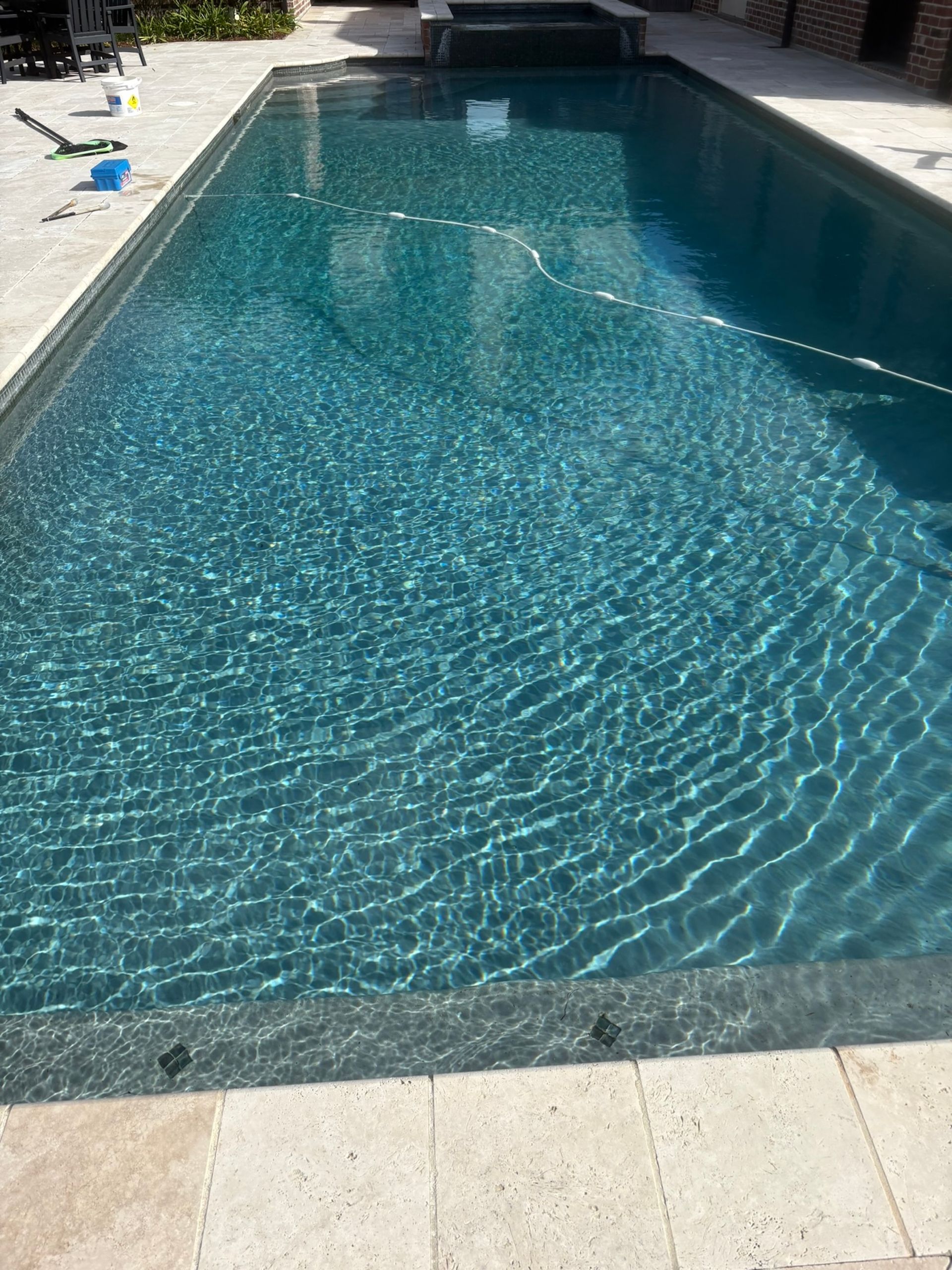 Rectangular swimming pool with turquoise water, surrounded by light-colored stone and brick.