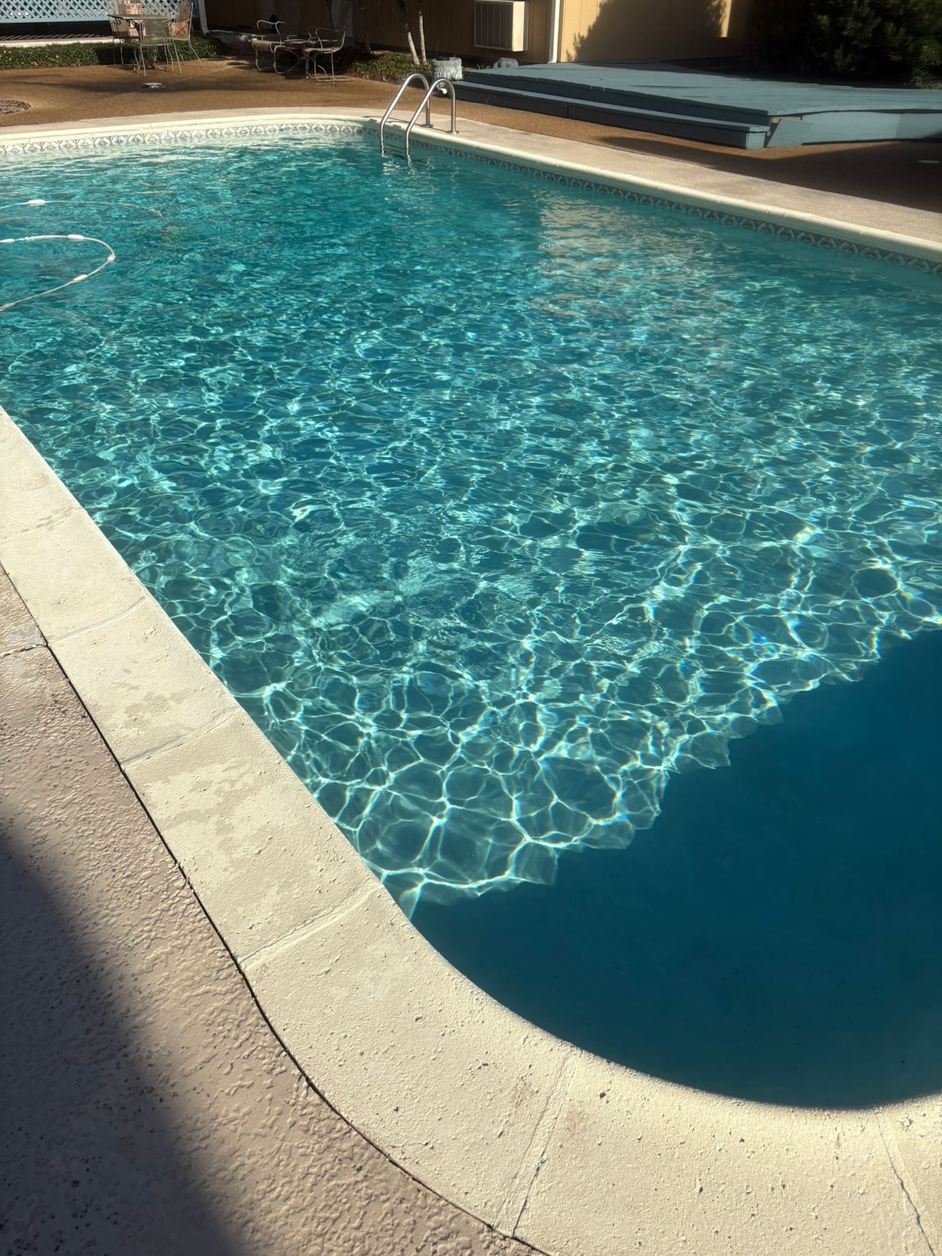 Rectangular swimming pool filled with shimmering turquoise water, concrete coping, sunny outdoor setting.