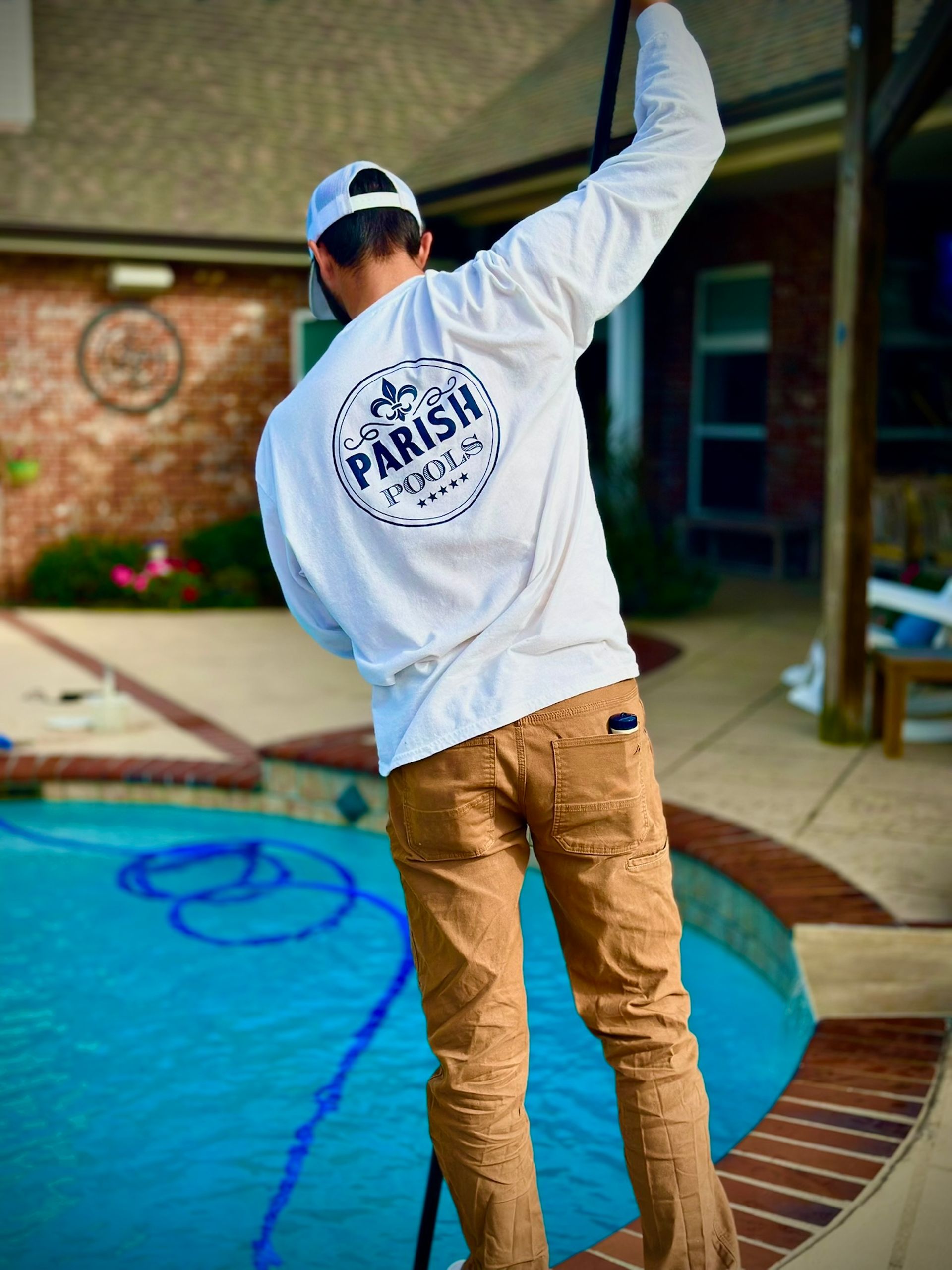 Person in white shirt and khaki pants cleaning a pool with the 