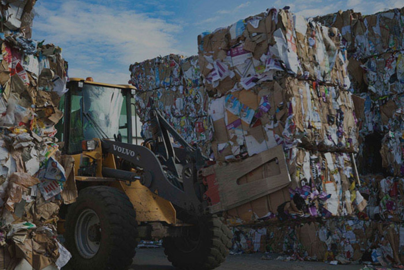 A bulldozer is moving a pile of cardboard boxes. A bulldozer is moving a pile of cardboard boxes.