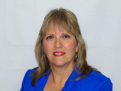 Woman in a blue blazer against a plain white background, facing forward with a slight smile