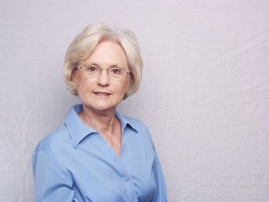 Portrait of a woman with short gray hair wearing a light blue shirt against a plain background