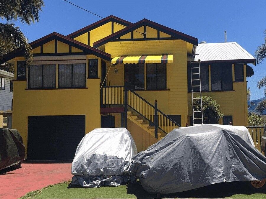 A Yellow House With Two Cars Parked In Front Of It — Pete's Painting Solutions In Cairns, QLD
