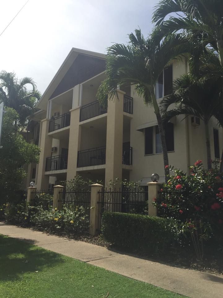 A large building with a fence and palm trees in front of it — Pete's Painting Solutions In Cairns, QLD