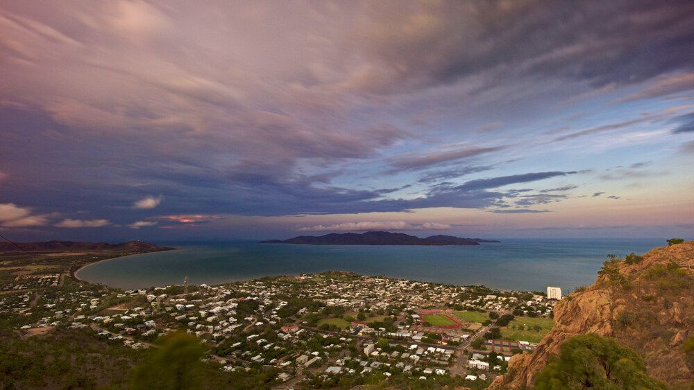 A View Of A City From A Cliff Overlooking The Ocean At Sunset — Pete's Painting Solutions In Bungalow, QLD